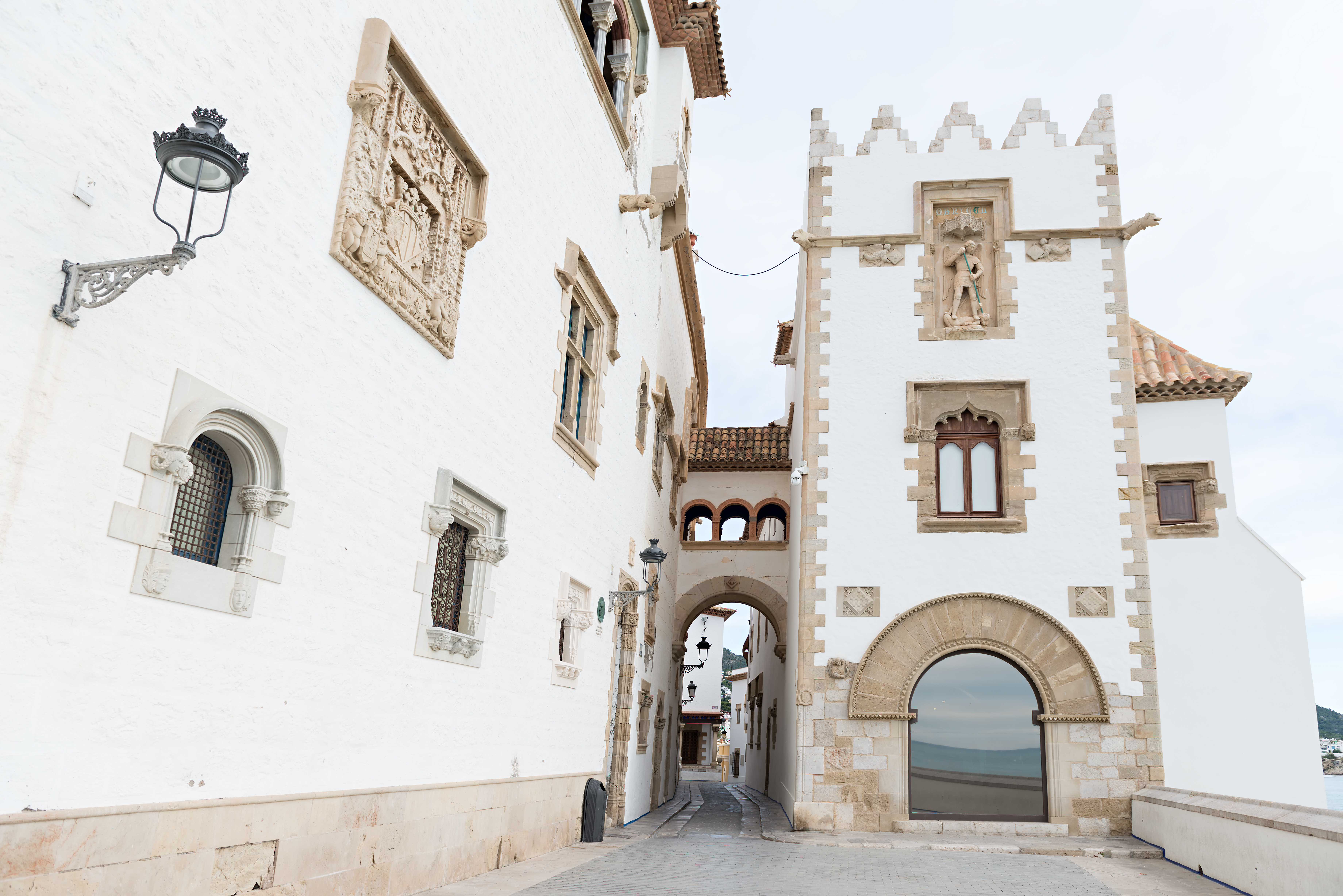 Callejón histórico en Sitges: edificios blancos, arcos y ventanas ornamentadas.