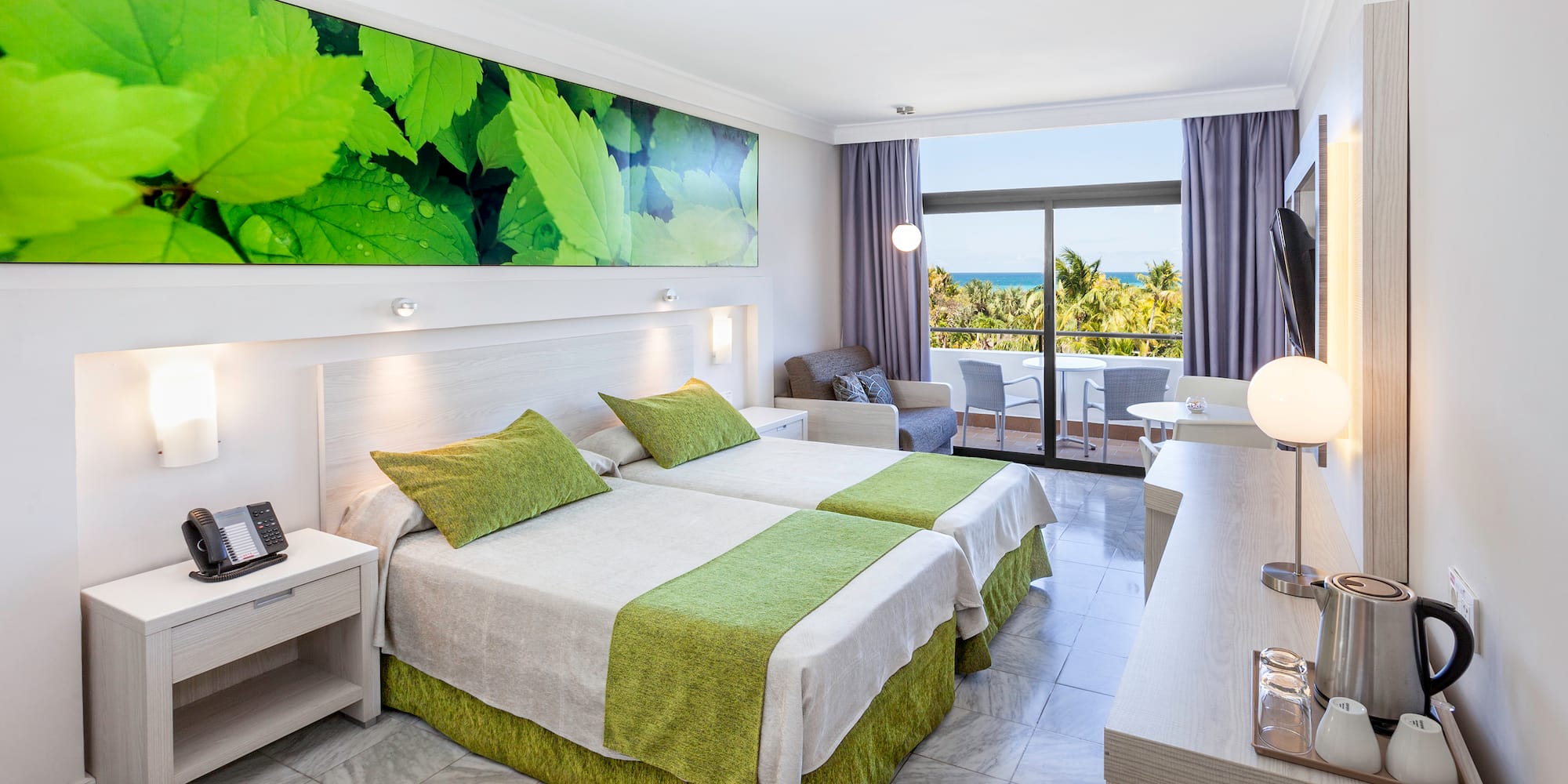 a room with two beds and a table with a window and a view of the ocean