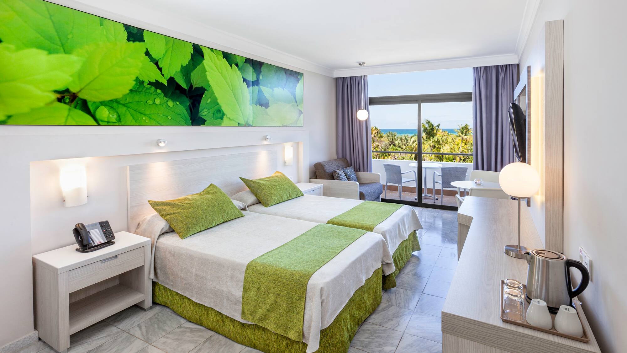 a room with two beds and a table with a window and a view of the ocean