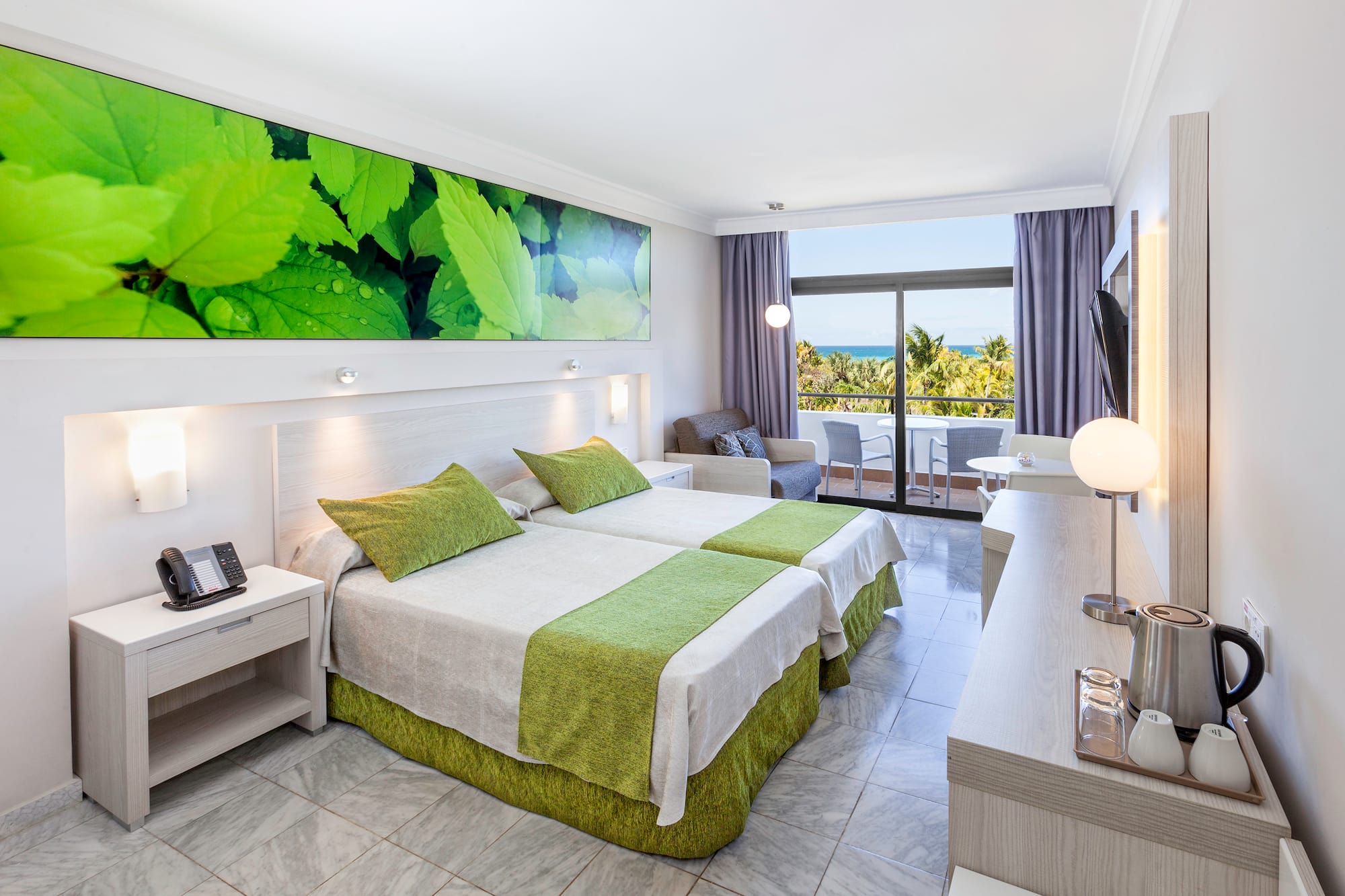 a room with two beds and a table with a window and a view of the ocean