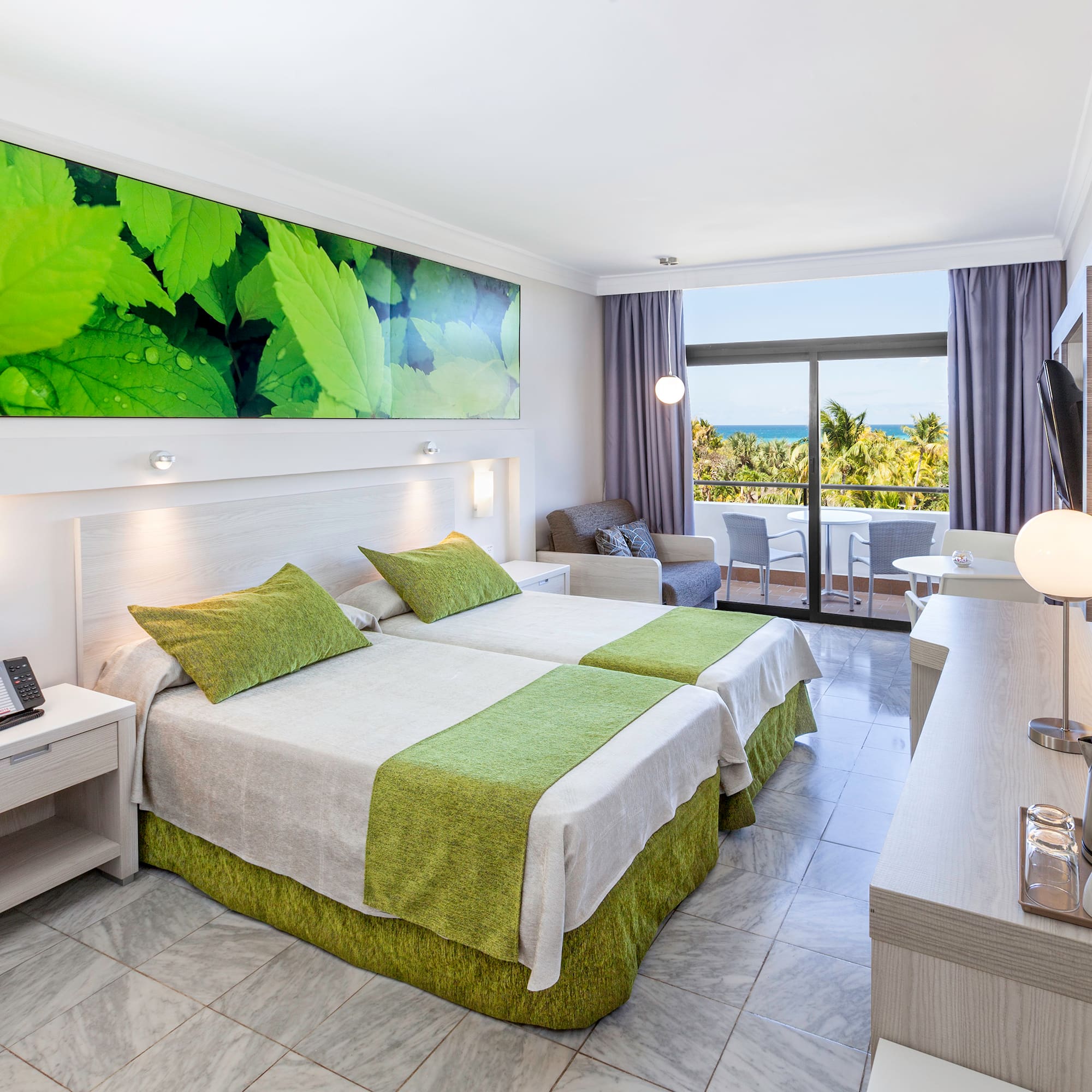 a room with two beds and a table with a window and a view of the ocean