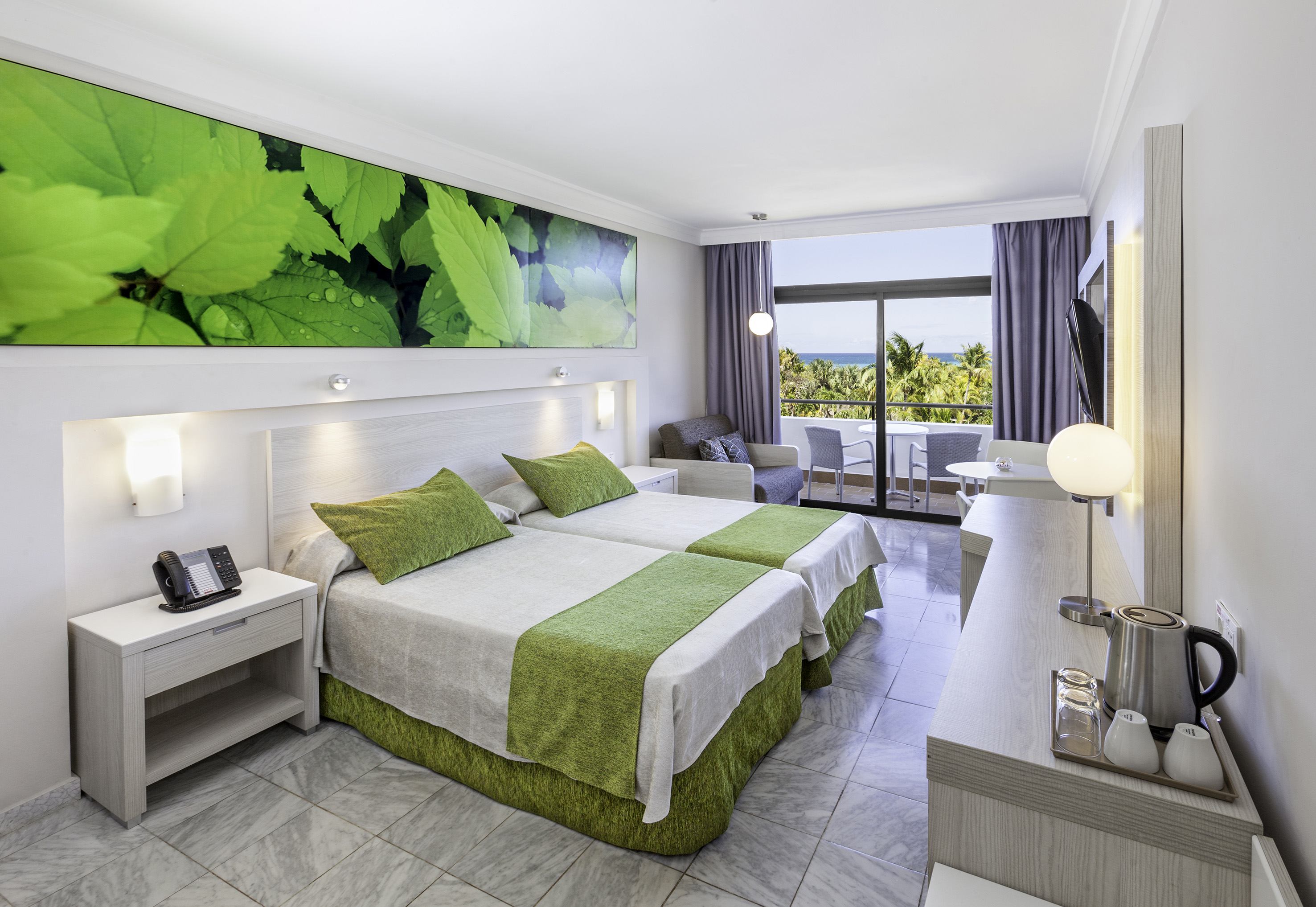 a room with two beds and a table with a window and a view of the ocean