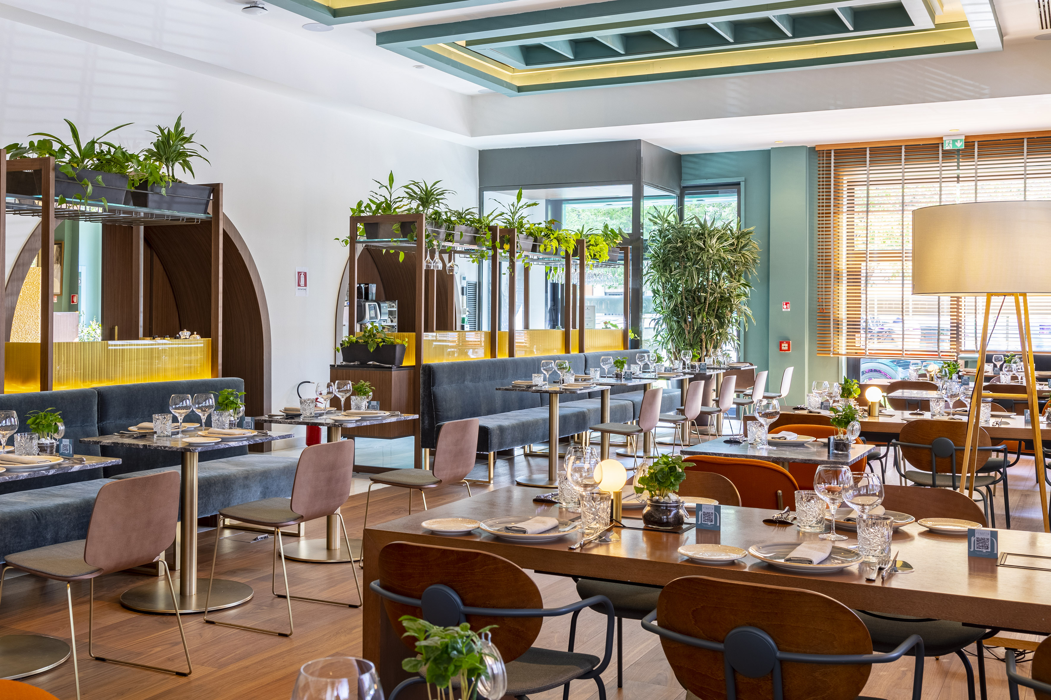 Stylish modern restaurant dining area with elegant tables, booths, and lush plants.