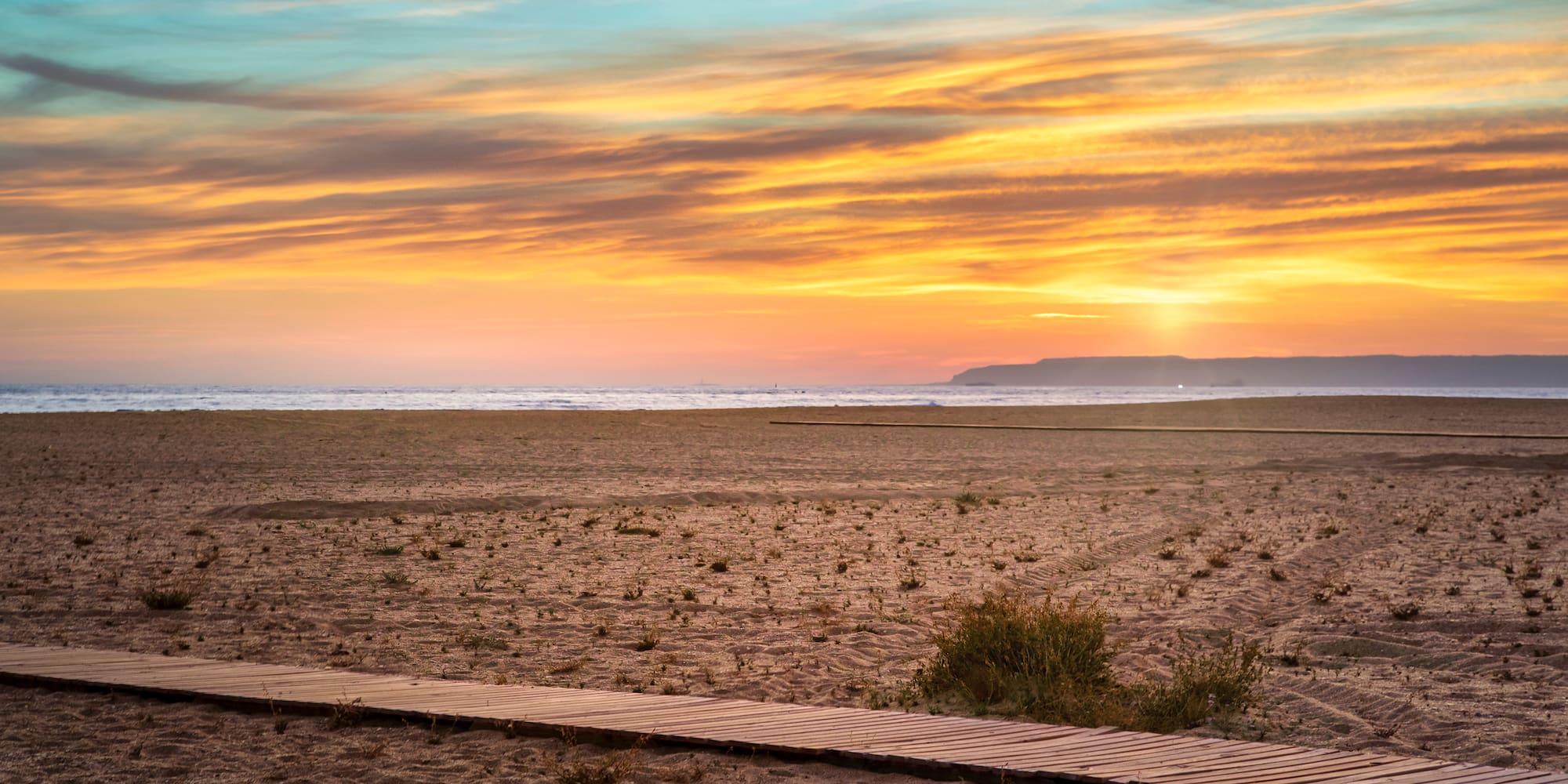 a beach with a wooden walkway and a sunset