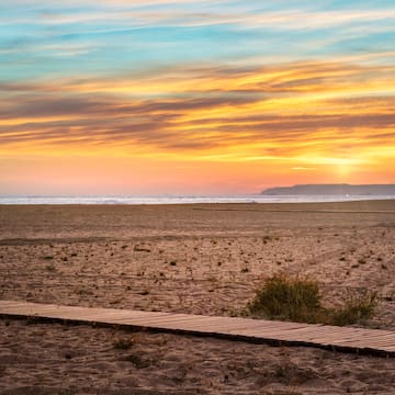 a beach with a wooden walkway and a sunset