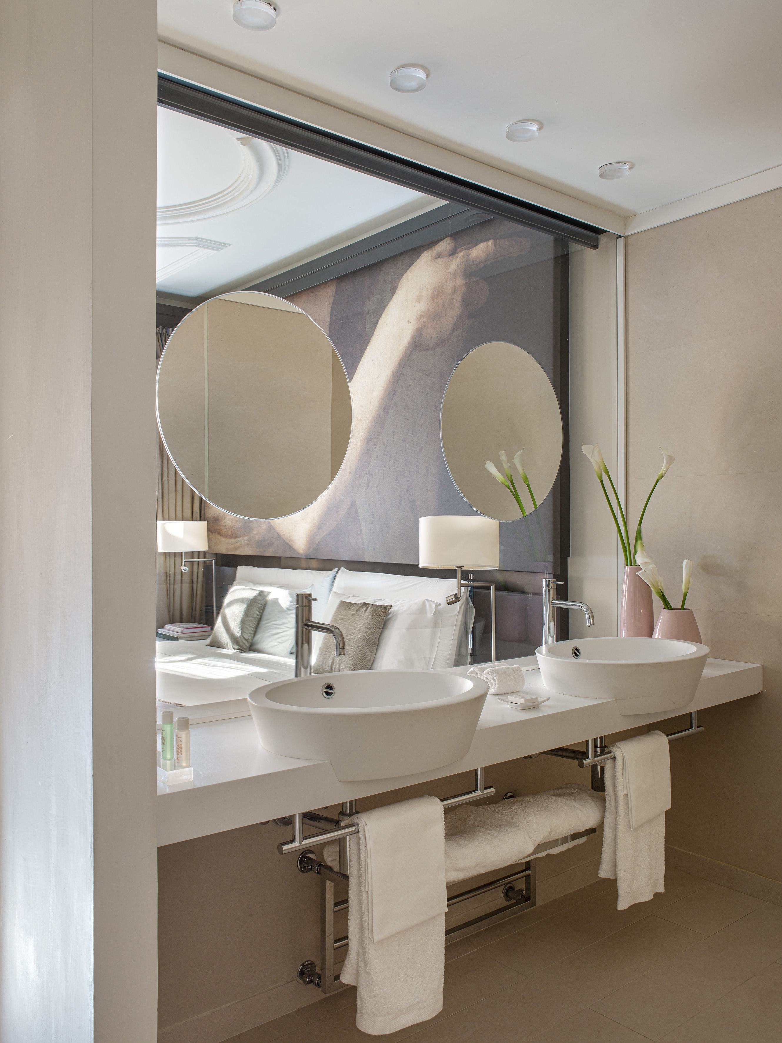 Modern dual vessel sinks, chrome faucets, white vanity, bedroom reflection.
