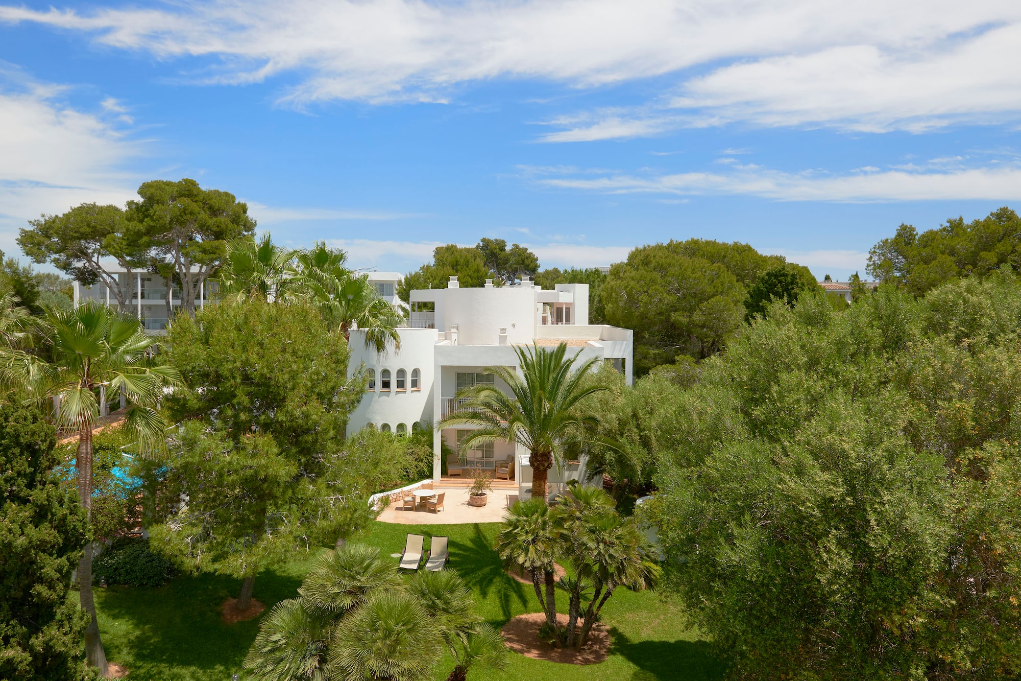 White Mediterranean villa nestled in lush palm gardens with outdoor patio.