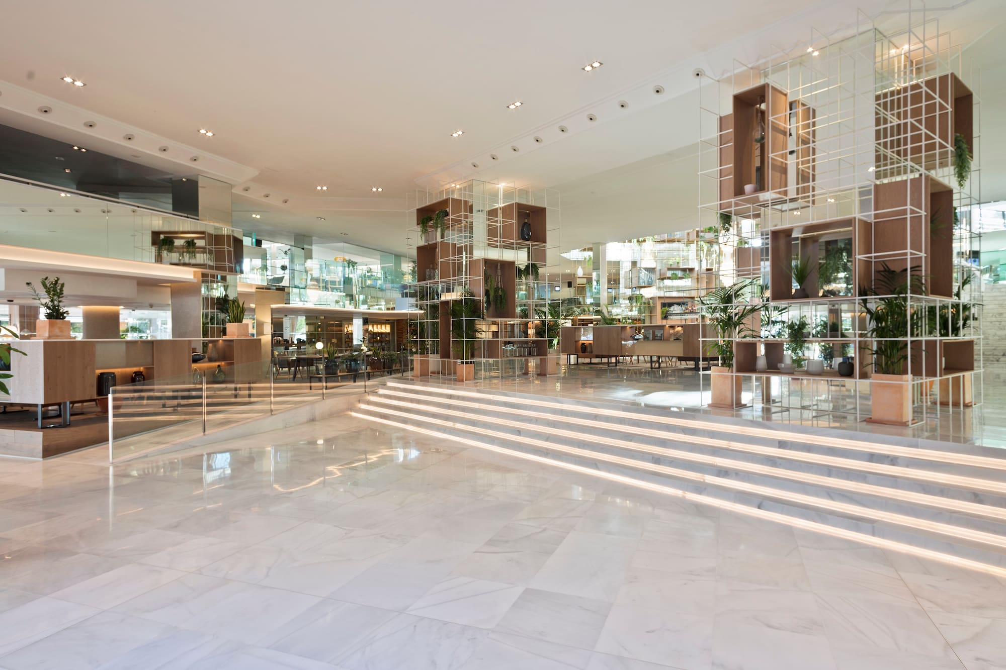 Modern hotel lobby with marble floor, illuminated steps, and plant decor.