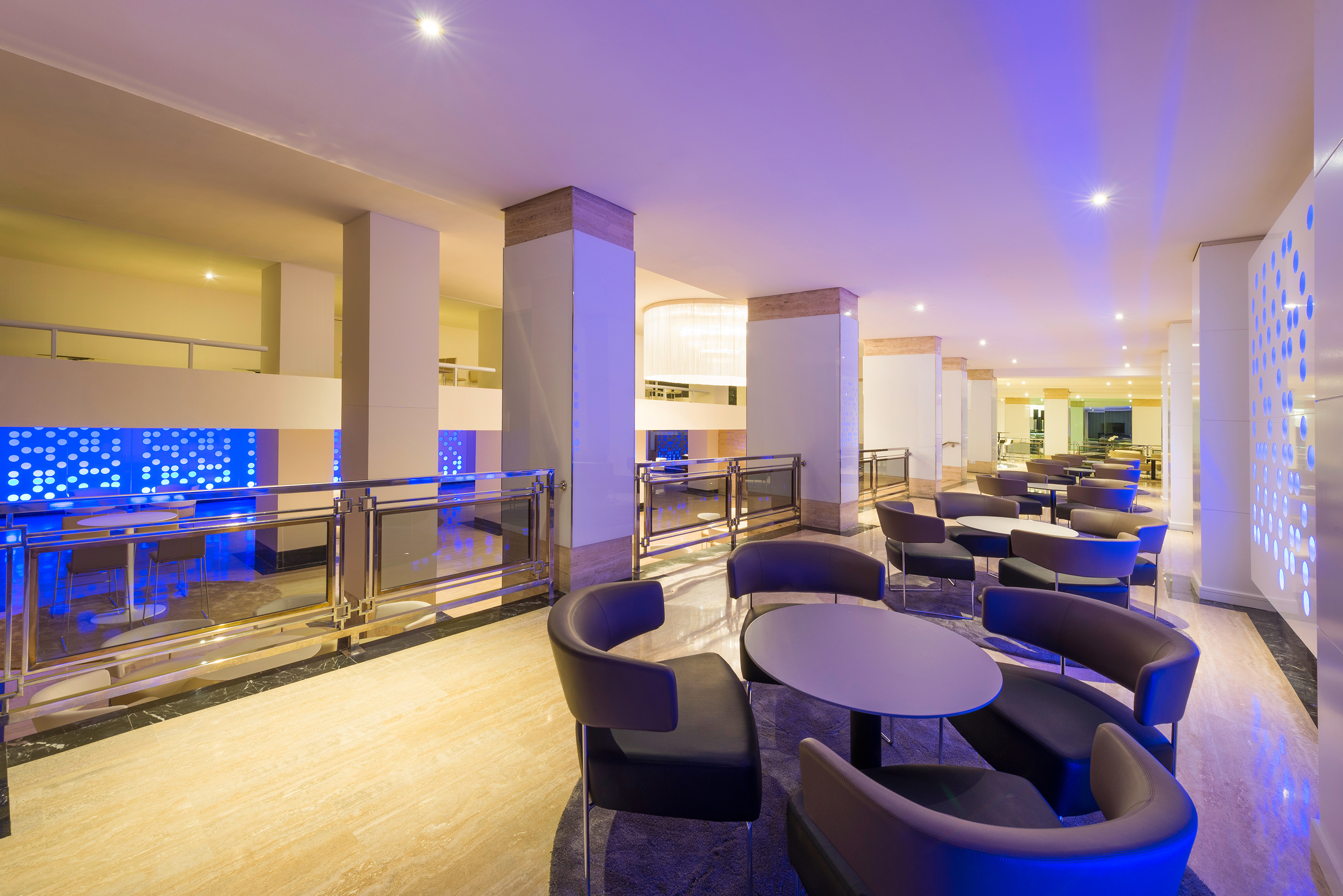 Modern hotel lobby lounge with blue accent lighting, sleek tables, and chairs.