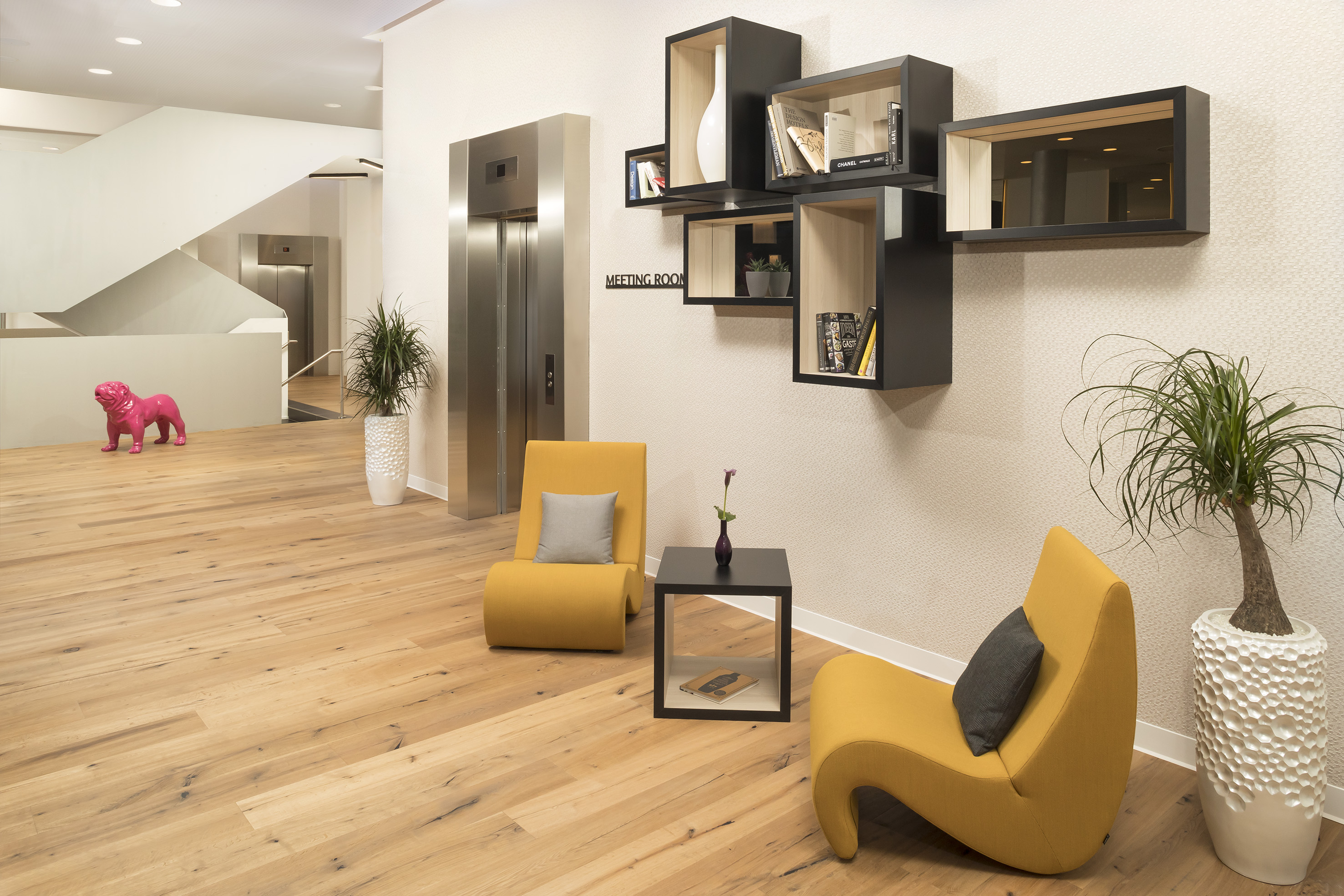 Modern reception with yellow chairs, wood floor, elevators, and pink bulldog art.