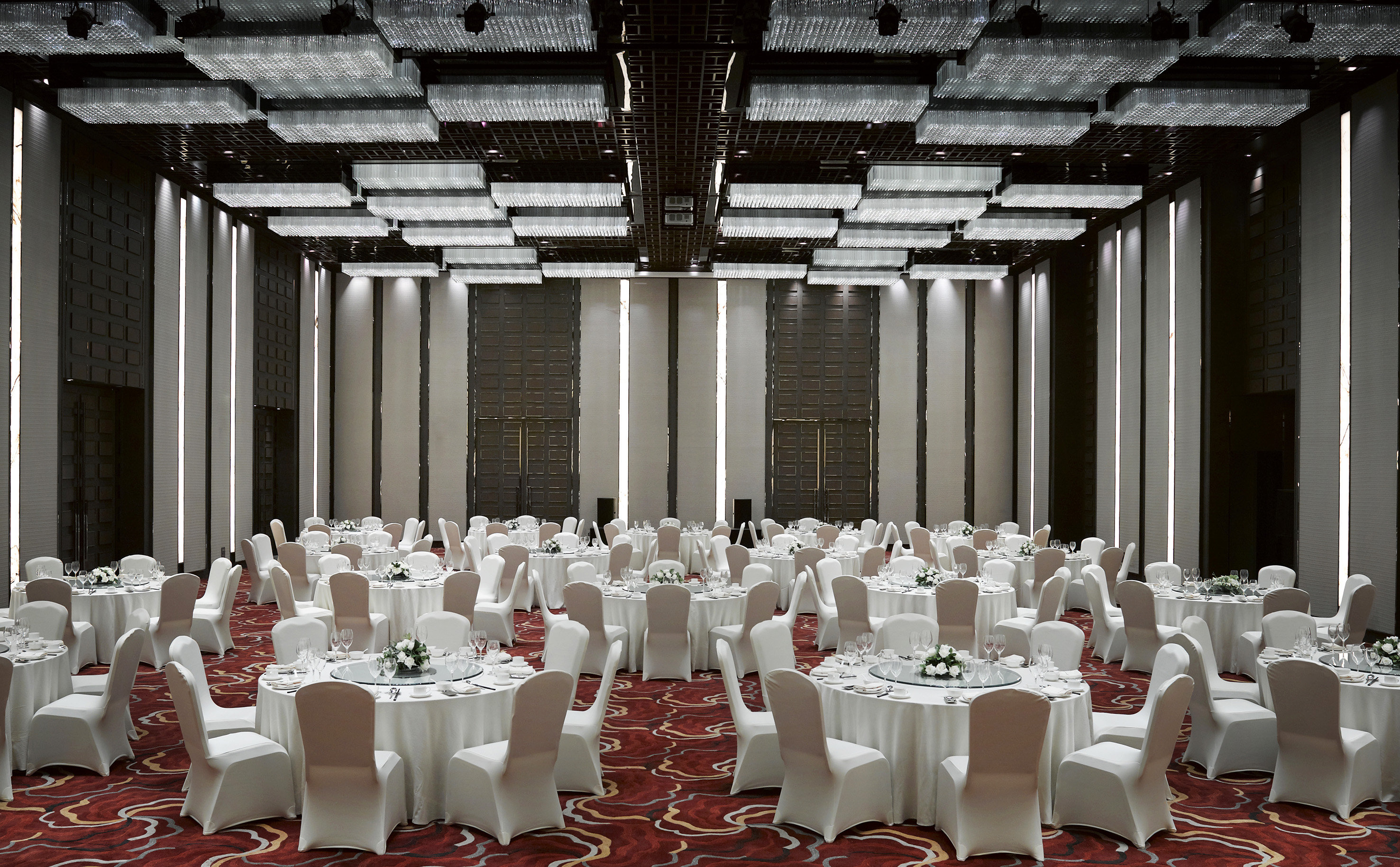 Elegant ballroom set for events with white round tables and modern chandeliers.