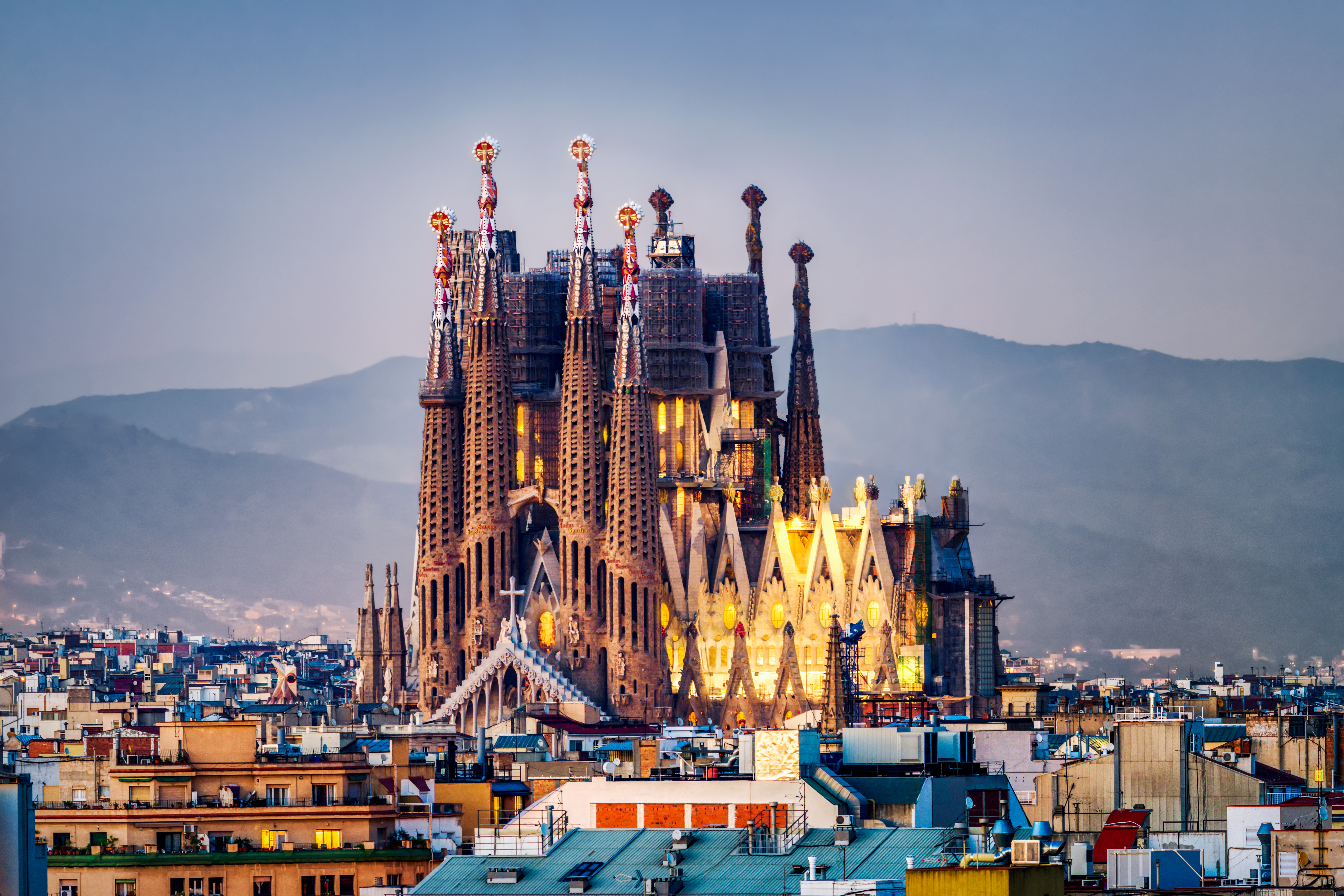 Sagrada Familia basilica illuminated at dusk over Barcelona's cityscape.