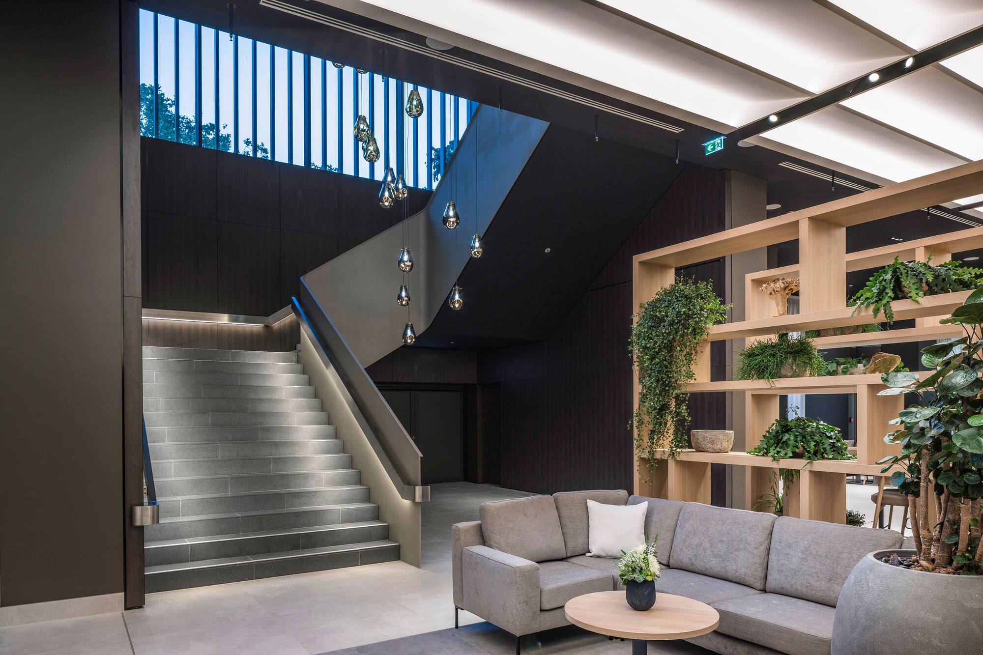 Modern office lobby, illuminated staircase, gray sofa, and green plant display.