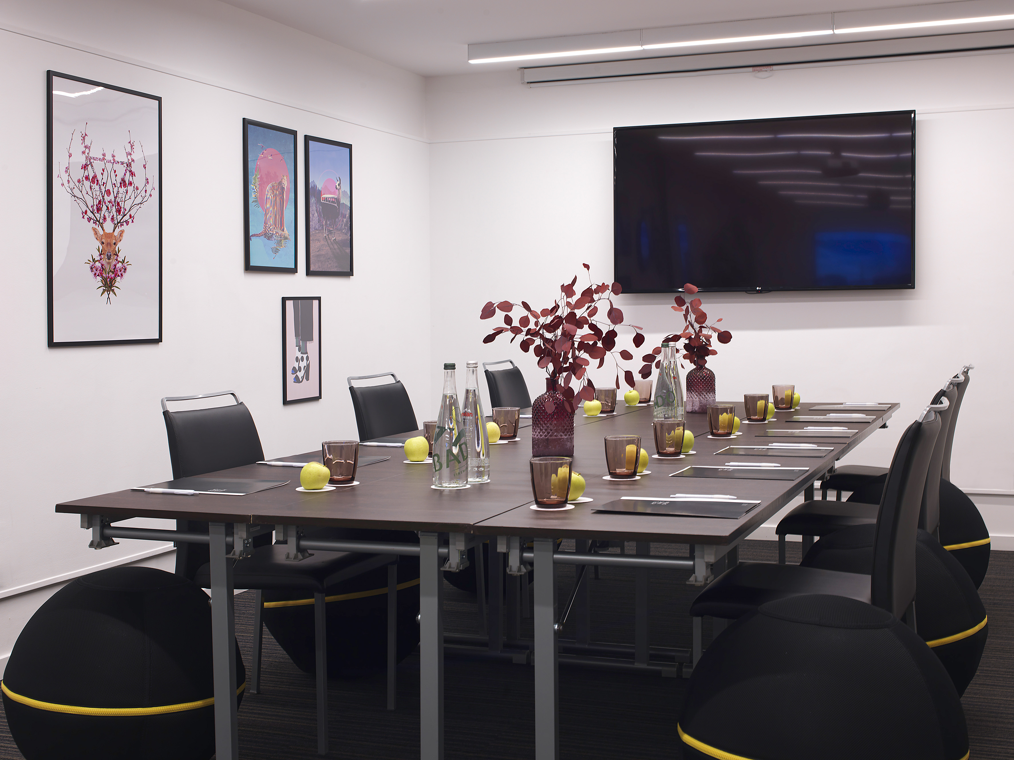 Modern meeting room with long table, TV, balance chairs, and framed wall art.