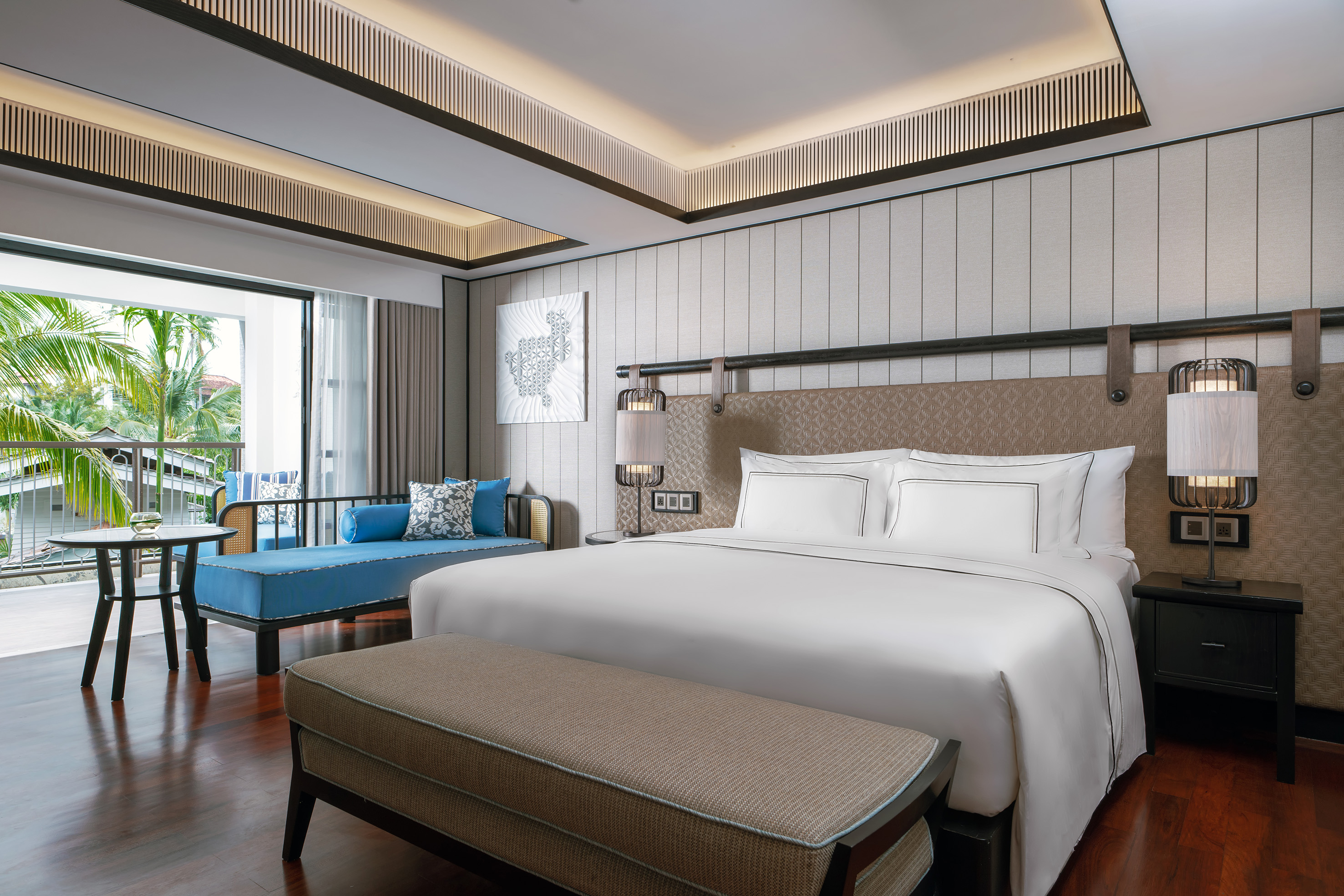 Luxury hotel bedroom with king bed, modern decor, and balcony offering a tropical view.