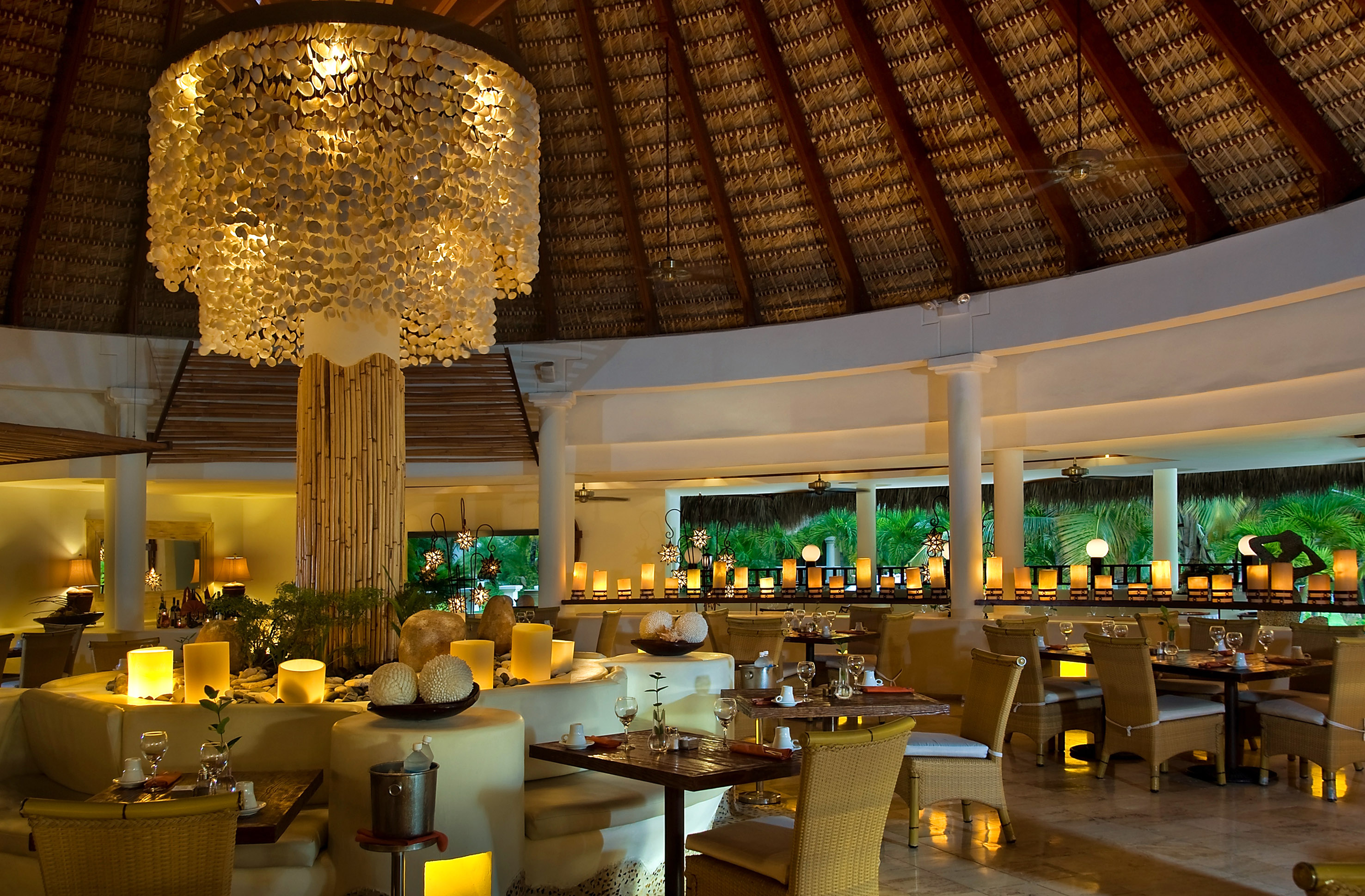 Tropical restaurant with glowing shell chandelier, thatched roof, and ambient lighting.
