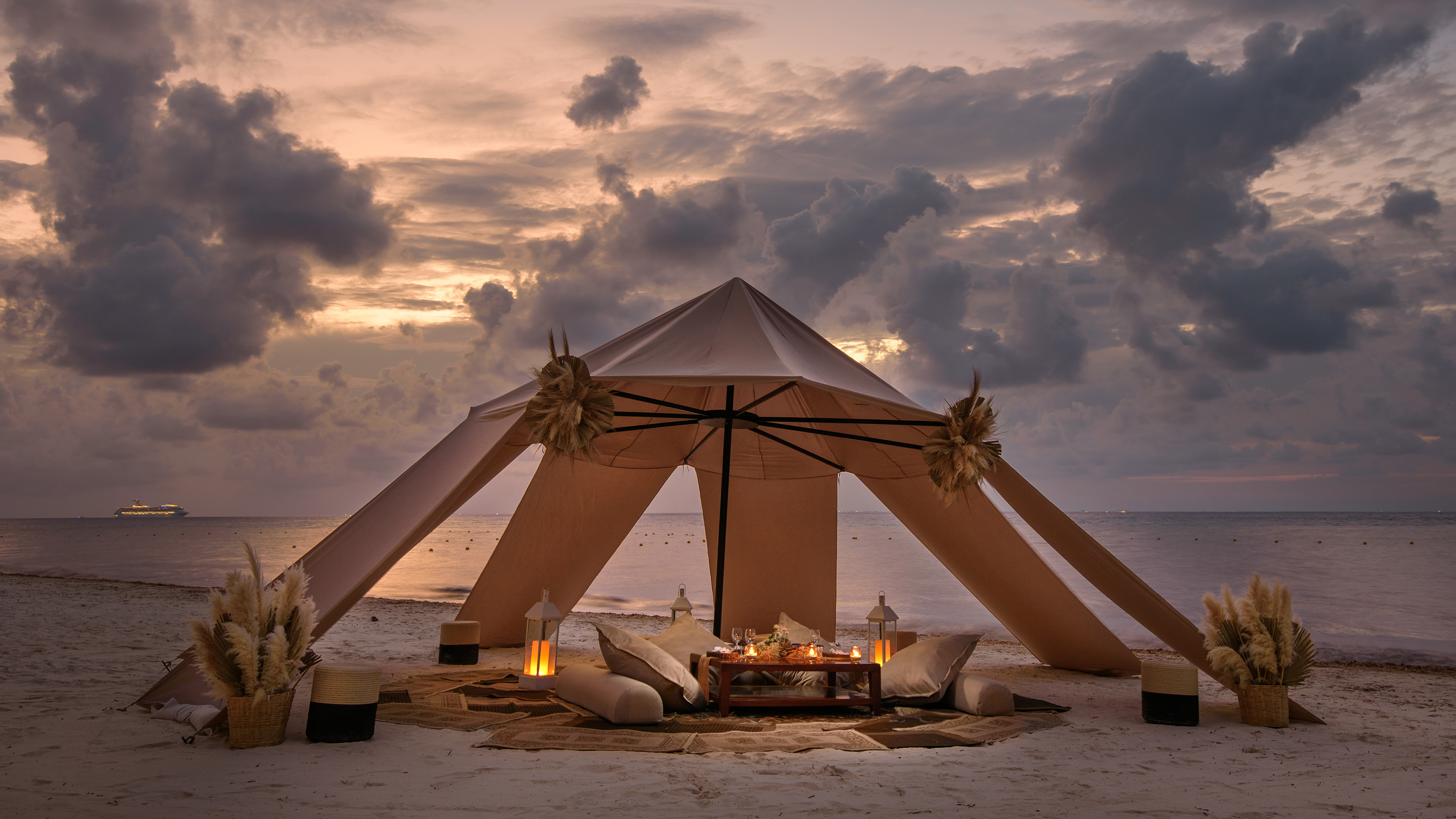Romantic beach dinner cabana with candles, sunset, and ocean view.