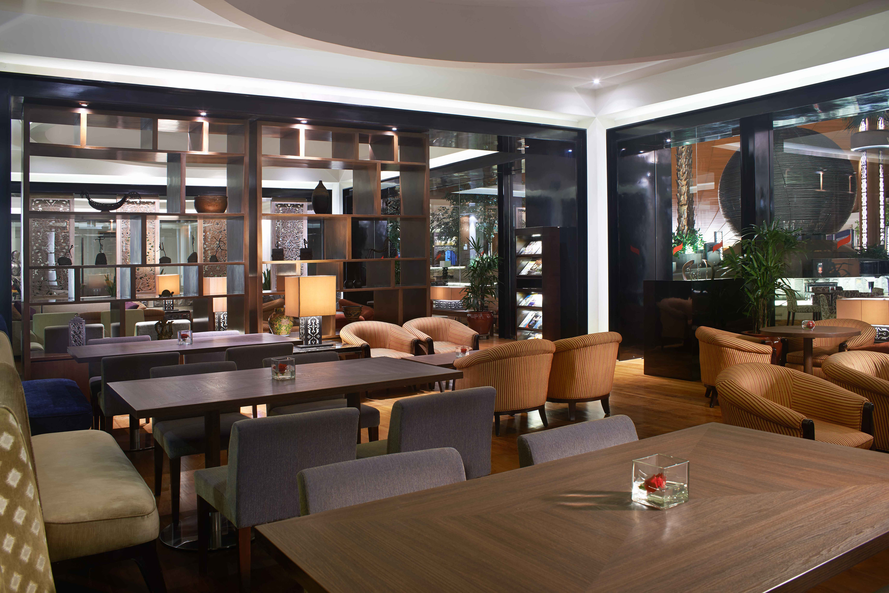 Modern hotel lounge interior with dark wood tables, gray chairs, and ambient lighting.