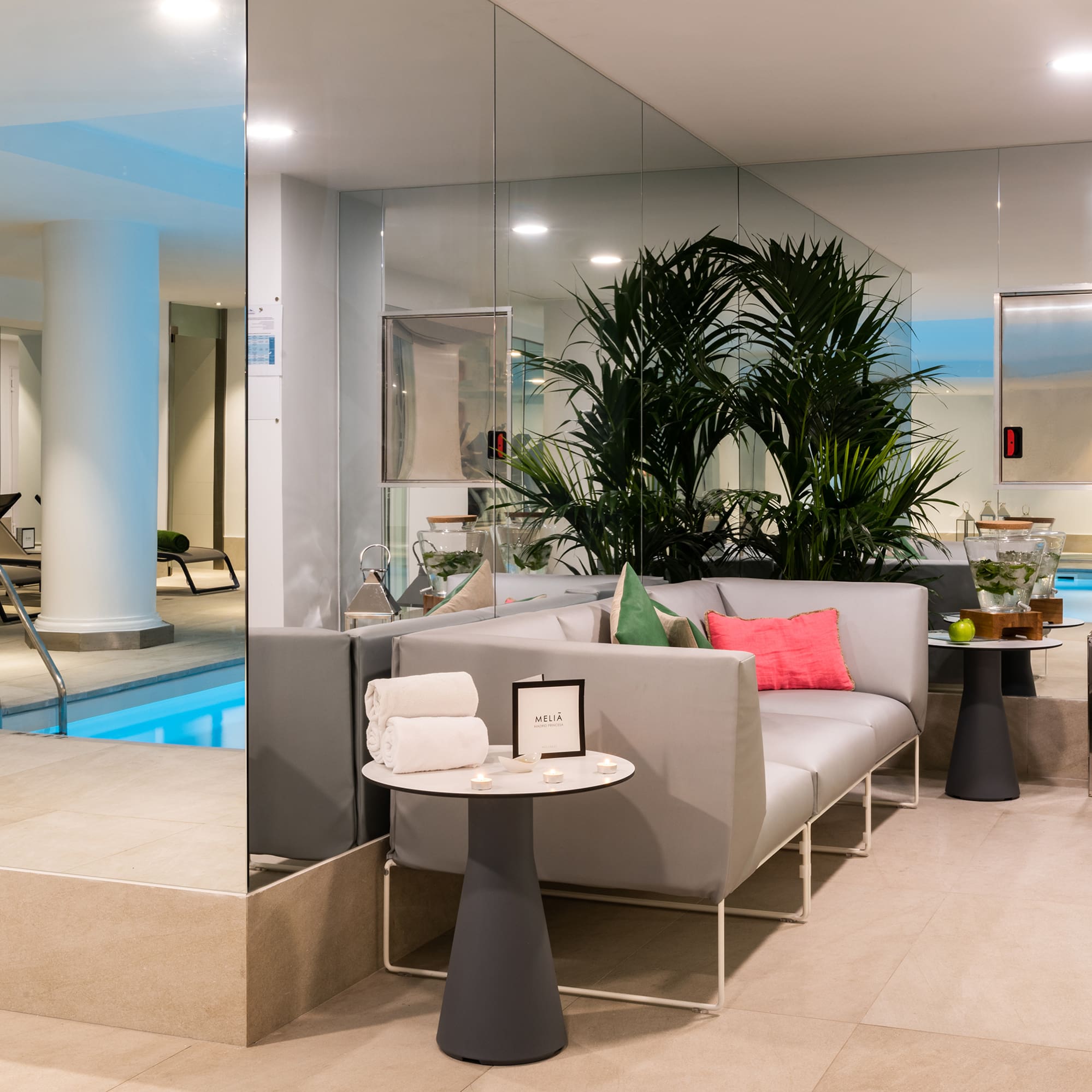 Relaxing indoor pool and spa lounge with modern sofa, lush plants, and mirrors.