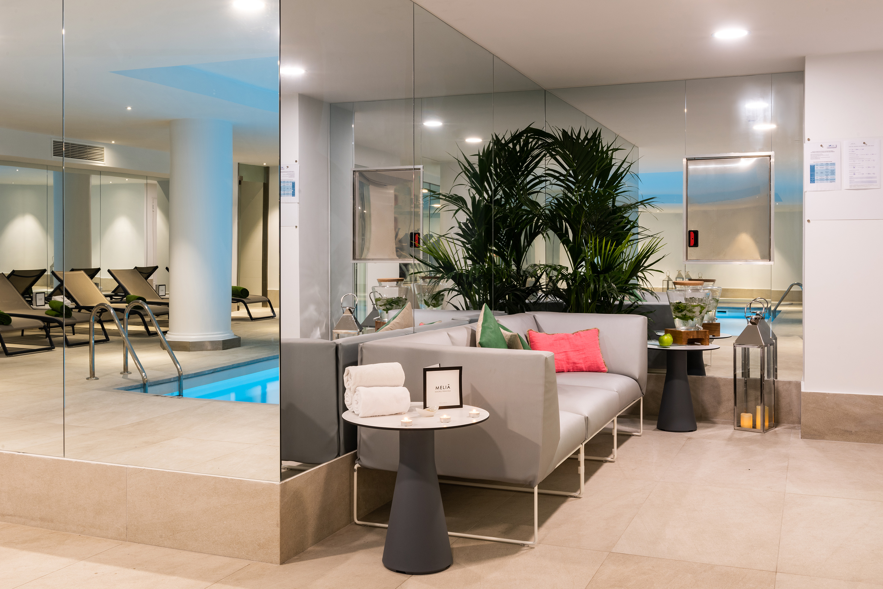 Relaxing indoor pool and spa lounge with modern sofa, lush plants, and mirrors.