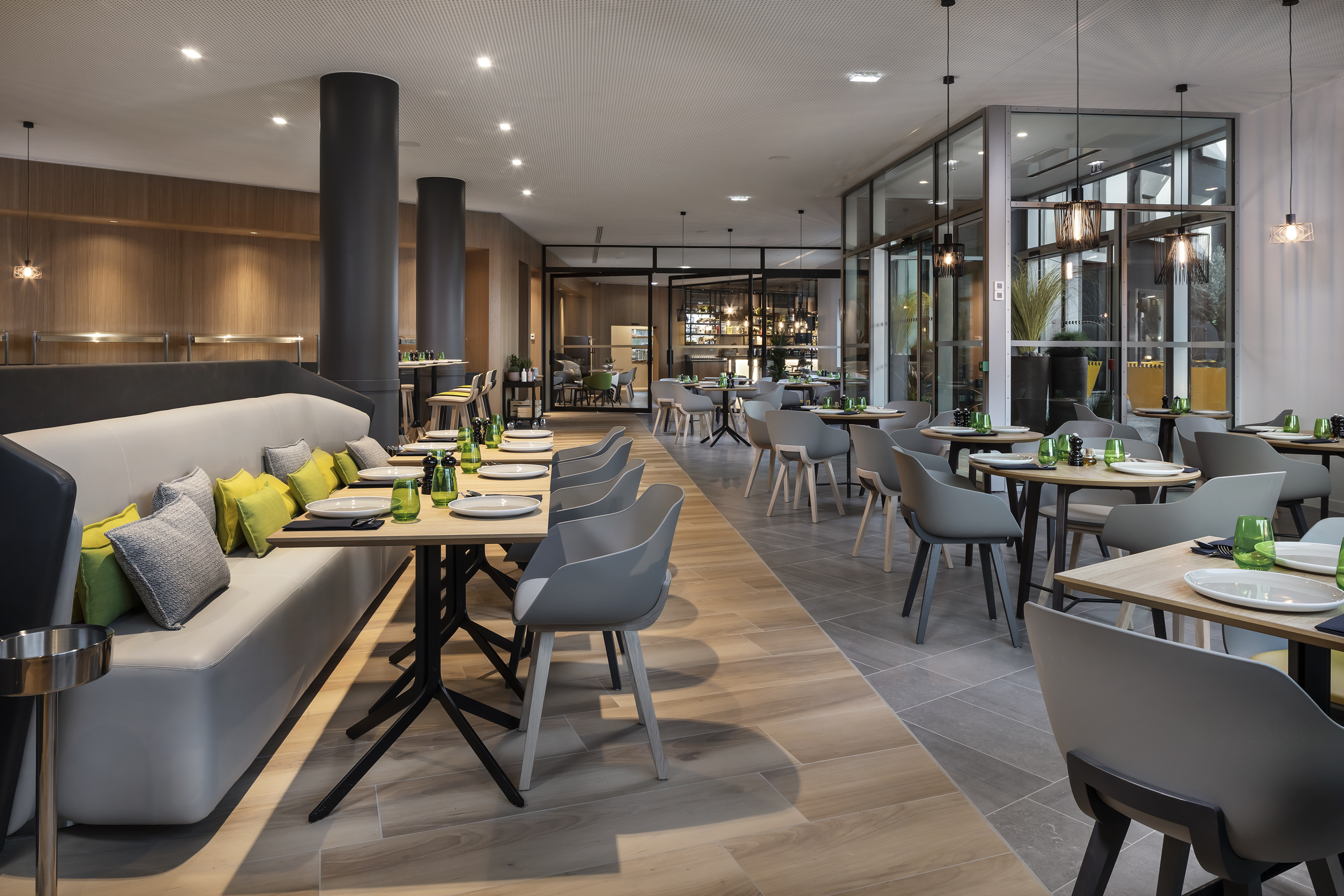 Modern restaurant dining room with set tables, grey chairs, and a long booth.