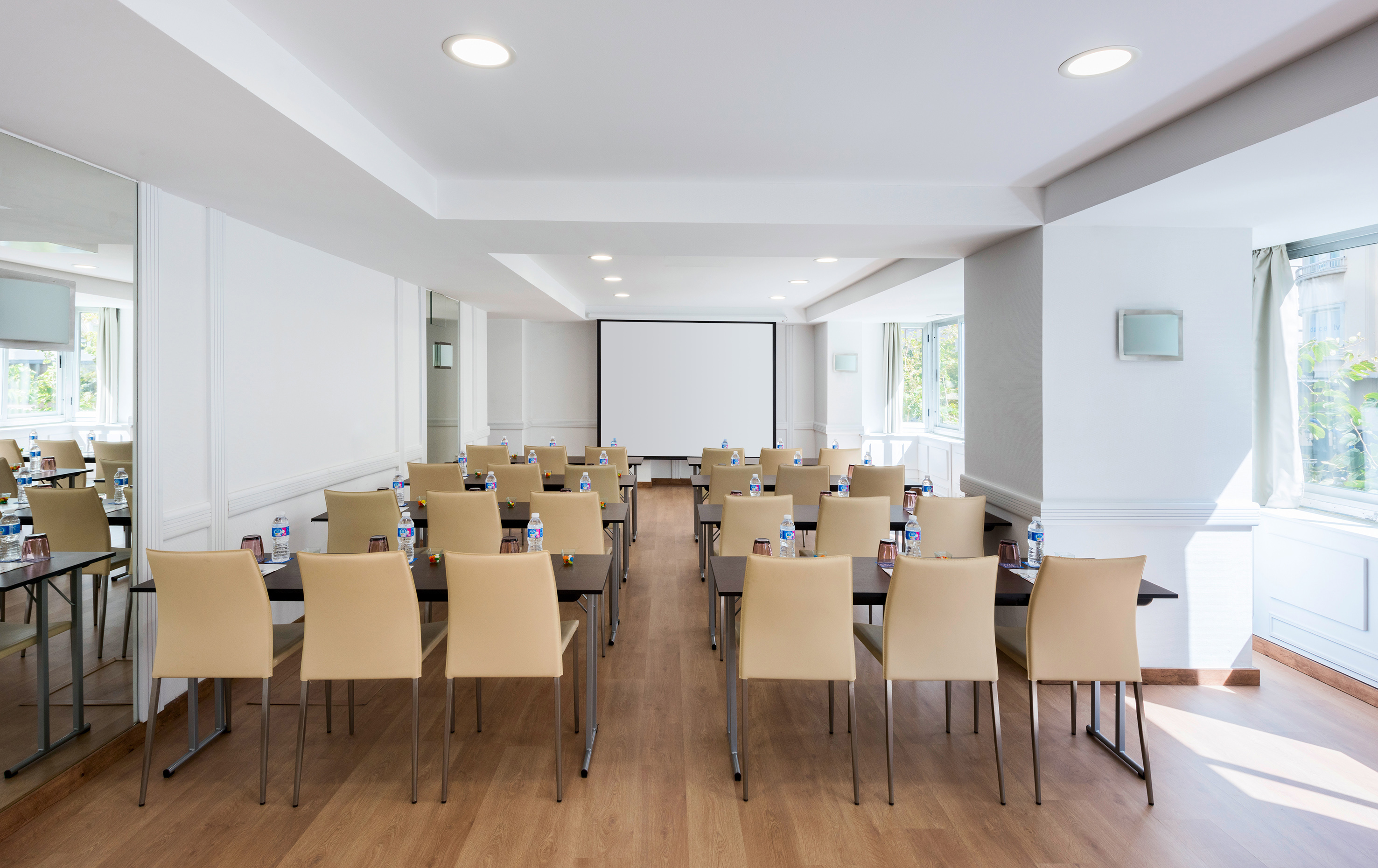 Bright conference room with tables, beige chairs, and a projection screen. - Postiguet - Hotel Alicante Gran Sol Affiliated by Meliá, 阿利坎特