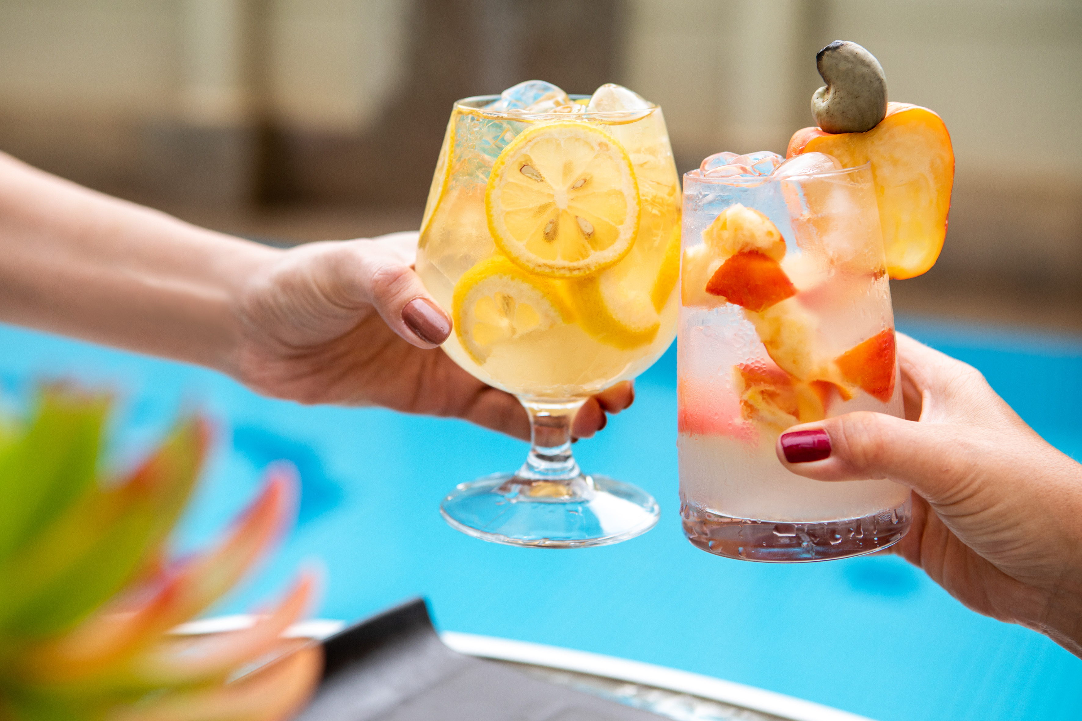 Hands toasting refreshing lemon and tropical cocktails poolside.