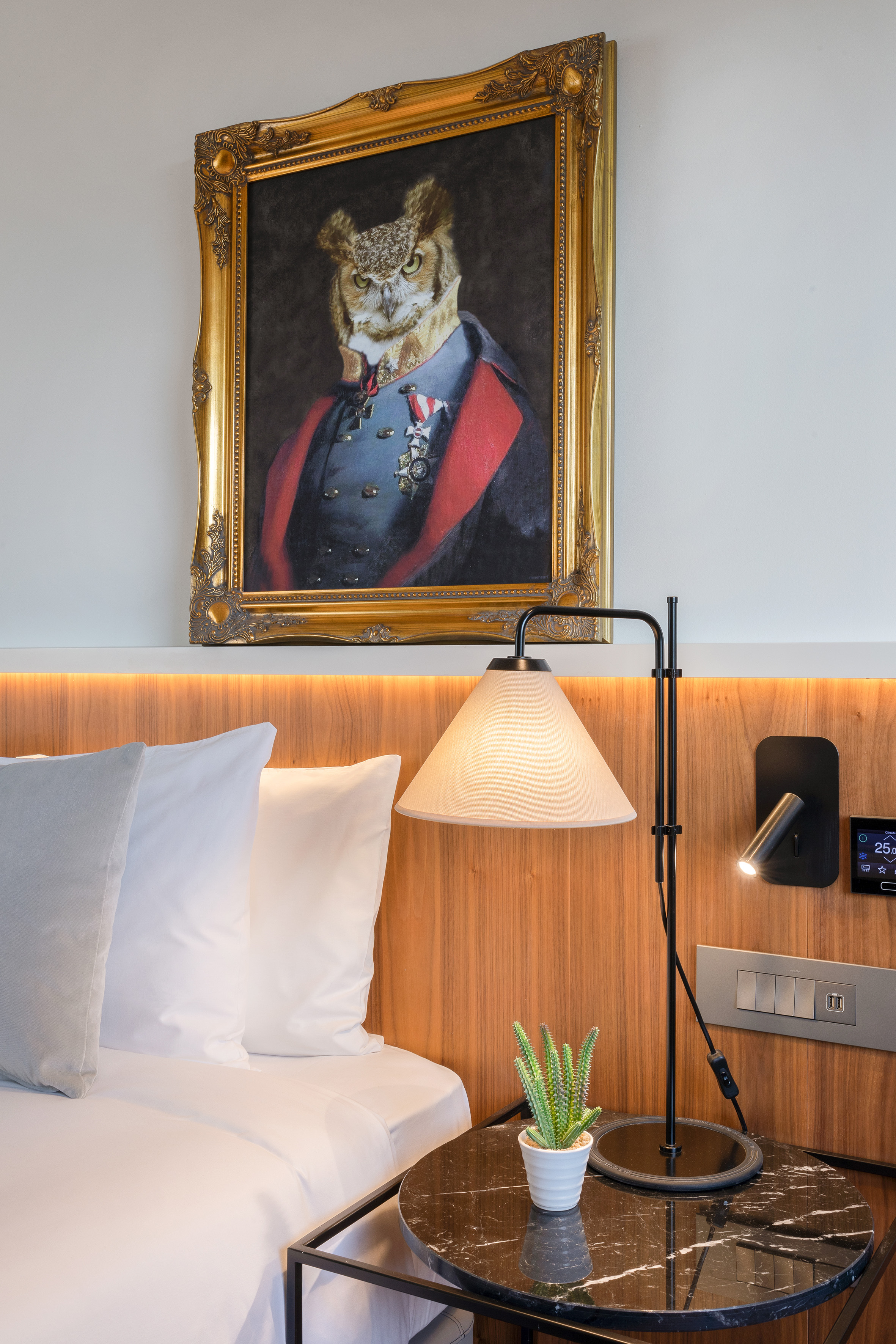 Ornate framed owl portrait in military uniform above a modern hotel bed.