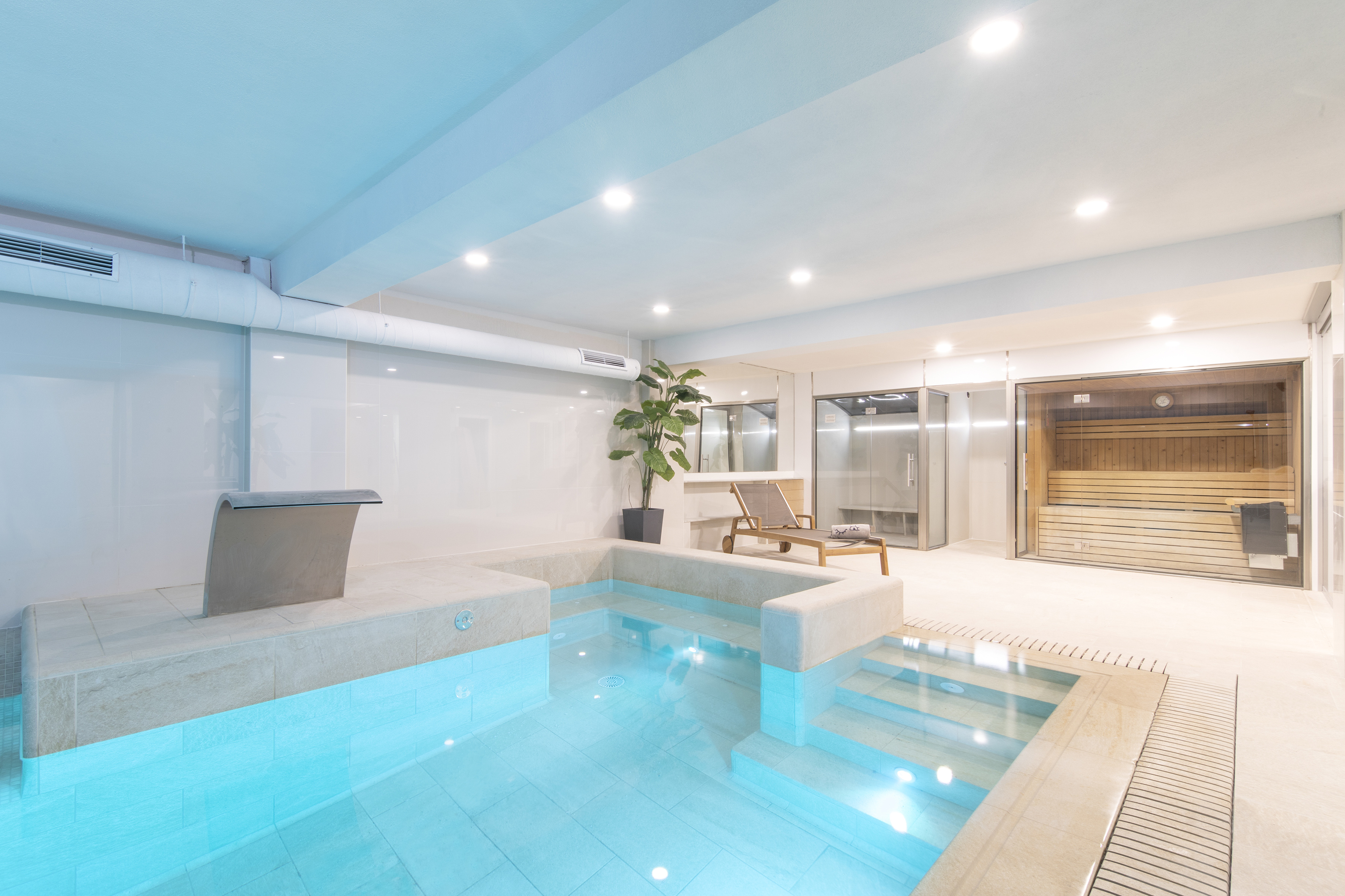 Modern wellness spa with bright blue indoor pool, sauna, and steam room.