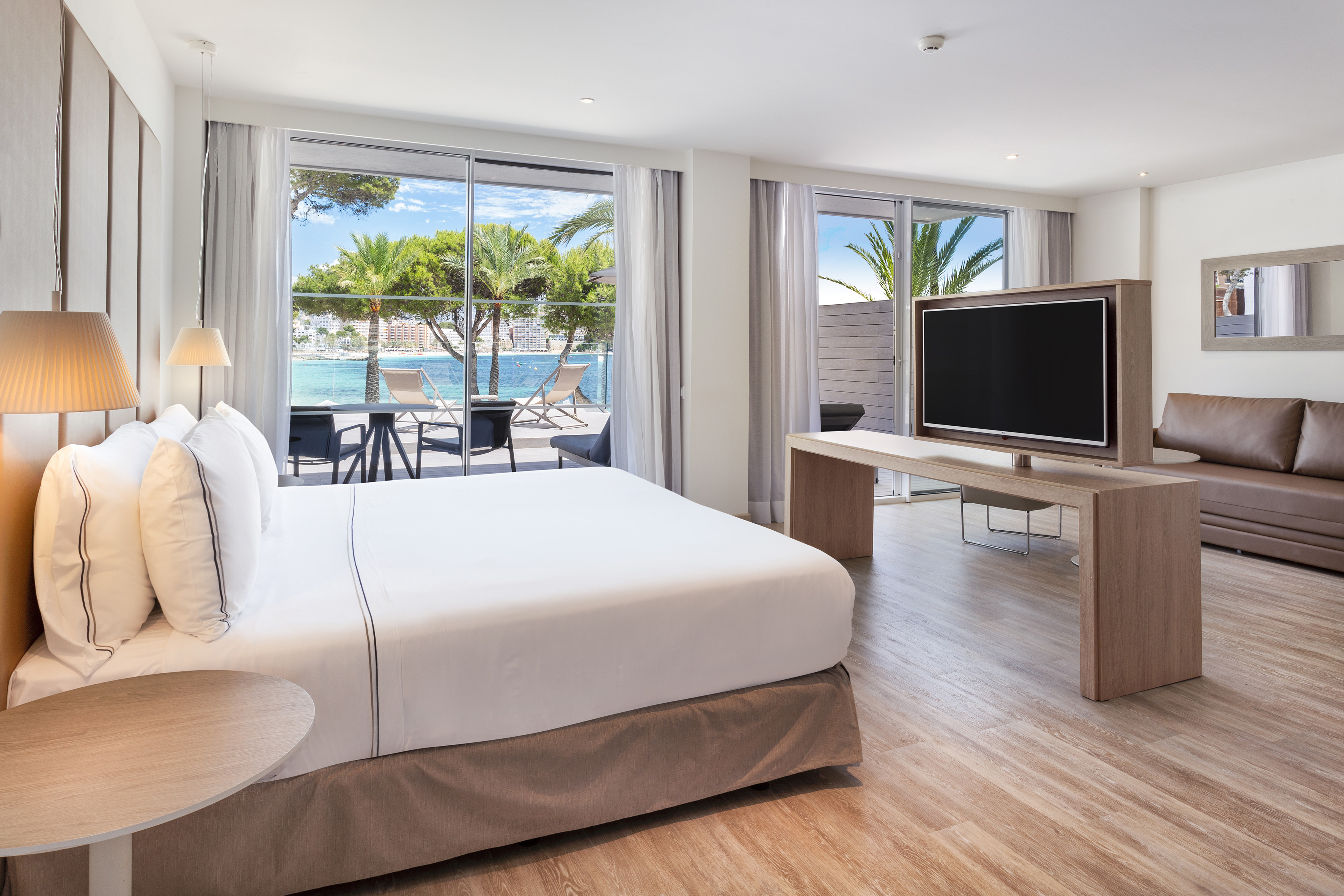 Modern hotel suite with ocean view balcony, large bed, and TV.