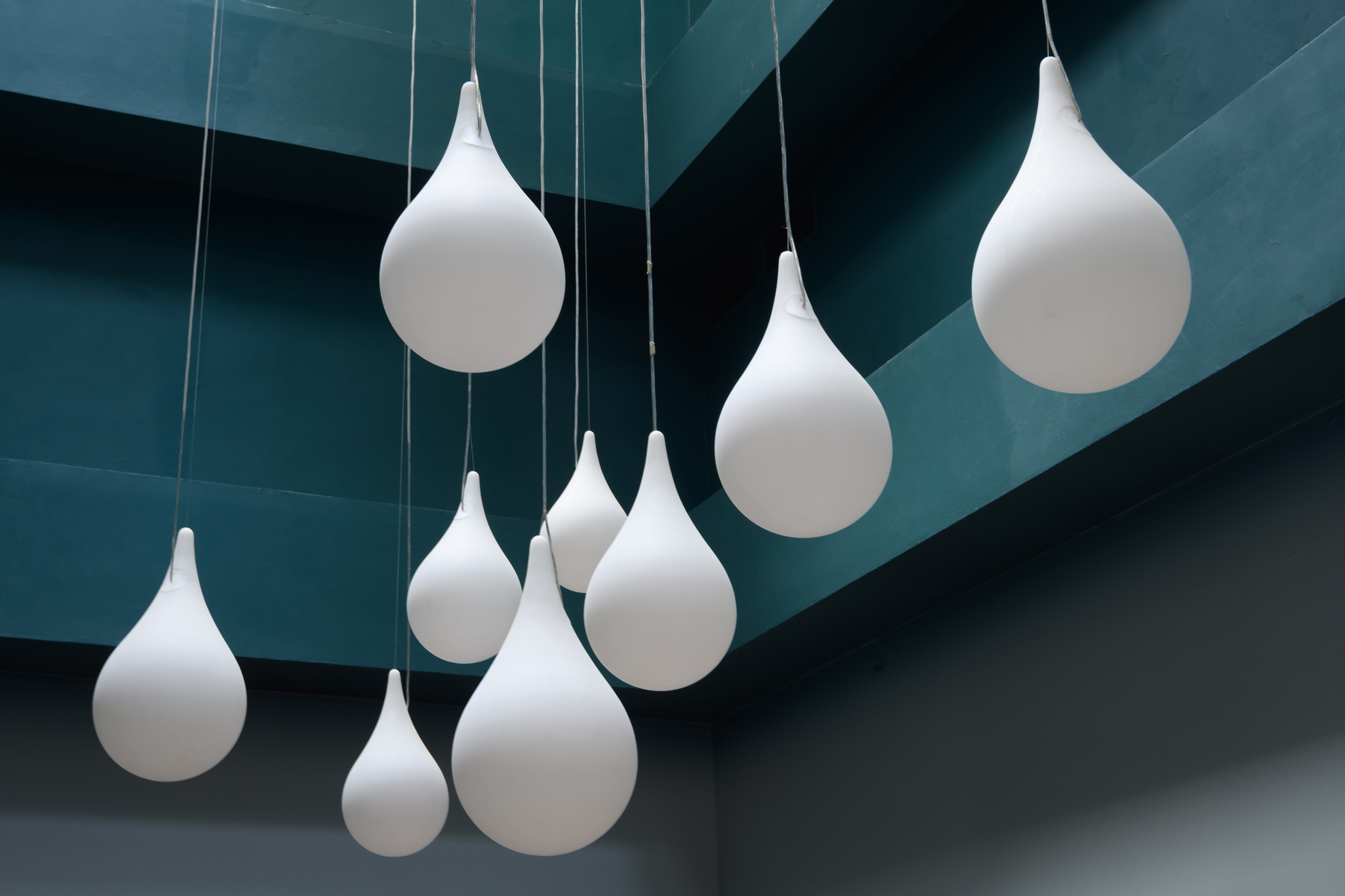 Modern white teardrop pendant lights suspended against a teal ceiling.