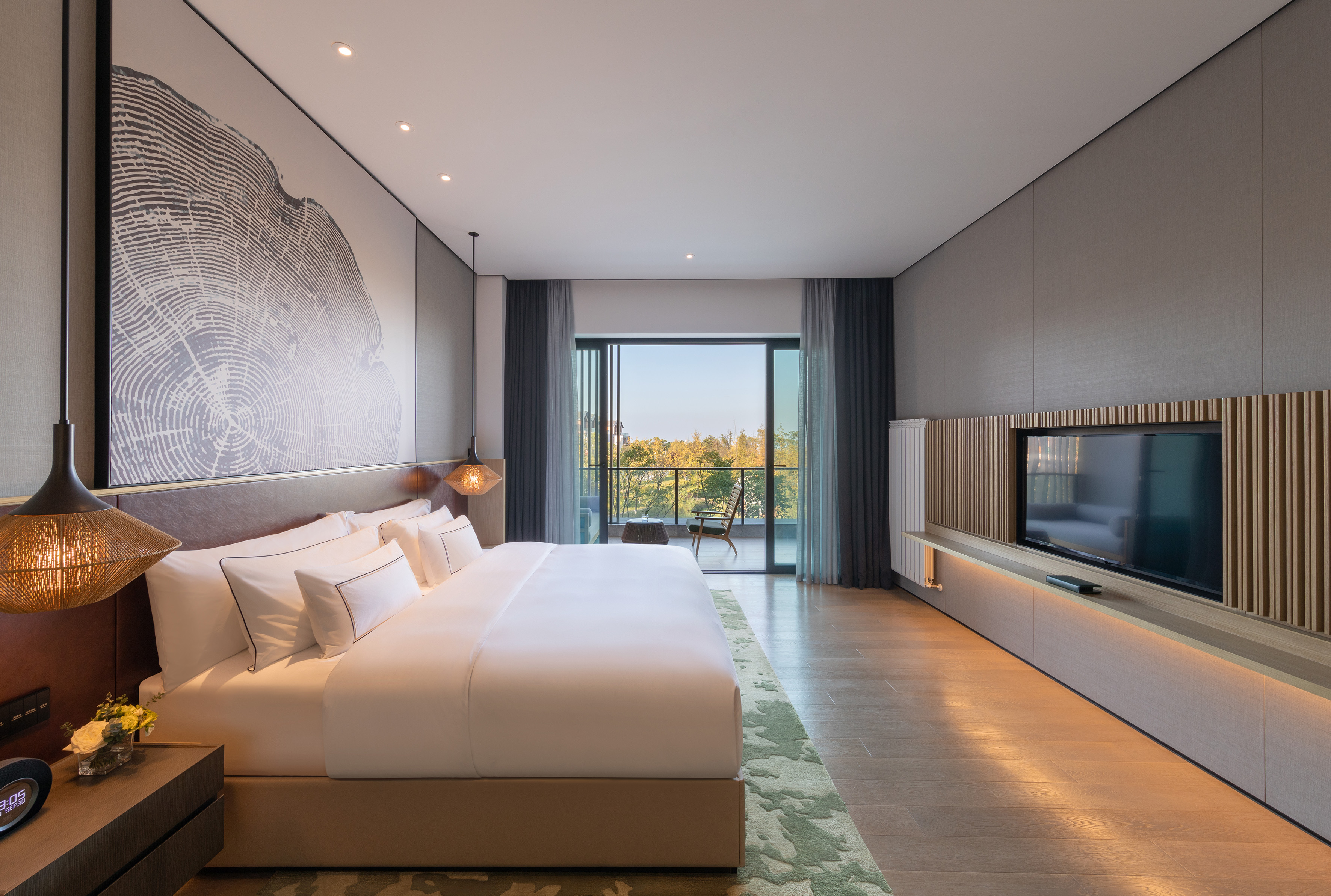 Modern hotel bedroom with tree ring art, large bed, and balcony forest view.
