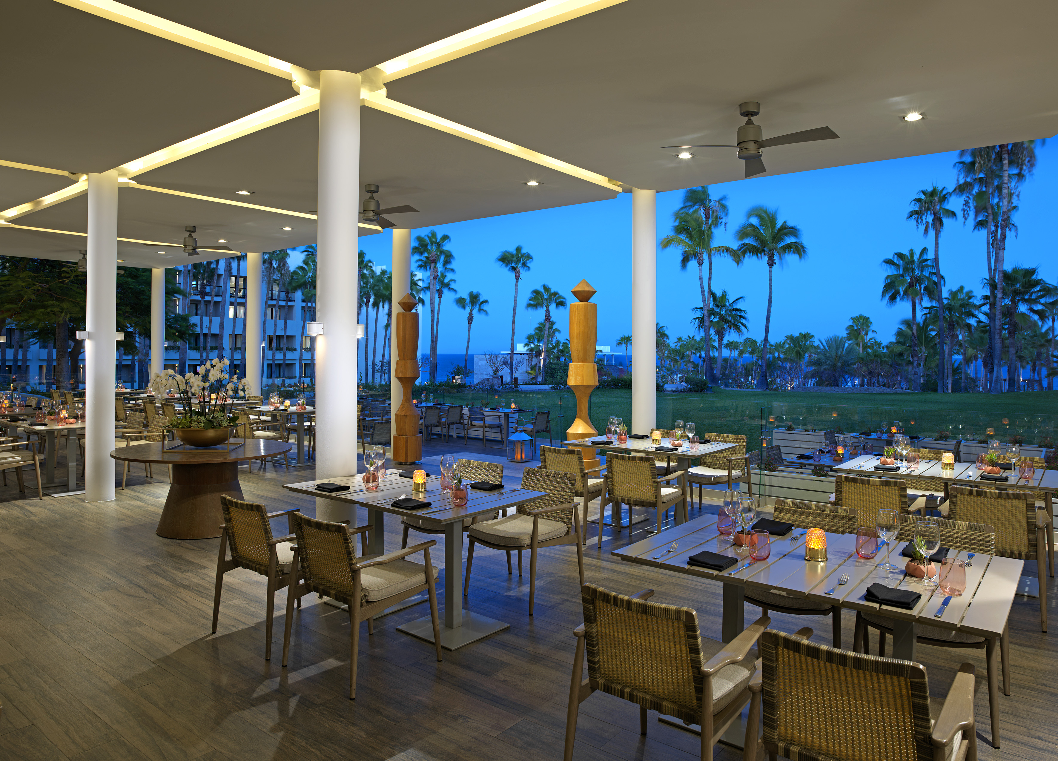 Elegant outdoor resort restaurant at dusk with set tables and palm trees.