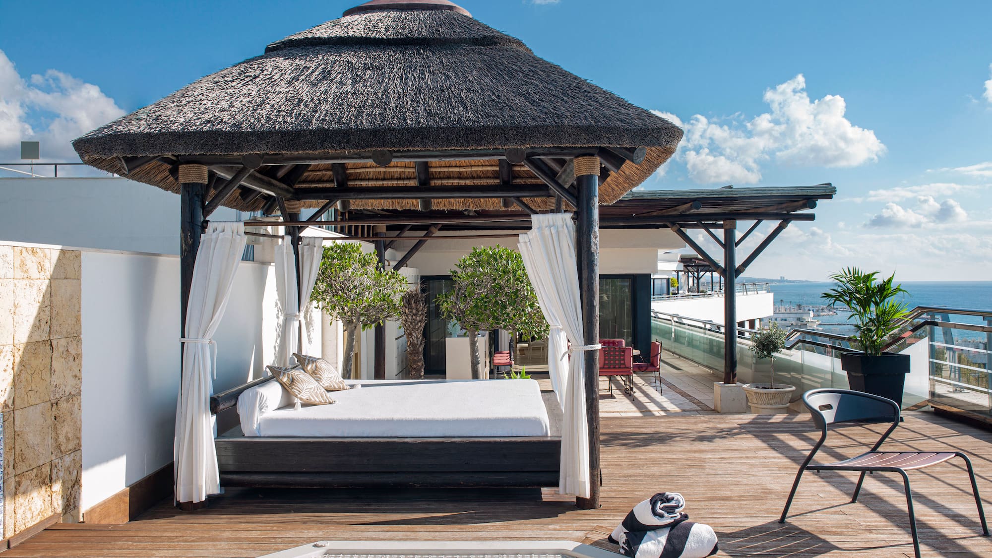 Luxury rooftop terrace with thatched gazebo daybed, hot tub, and ocean view.