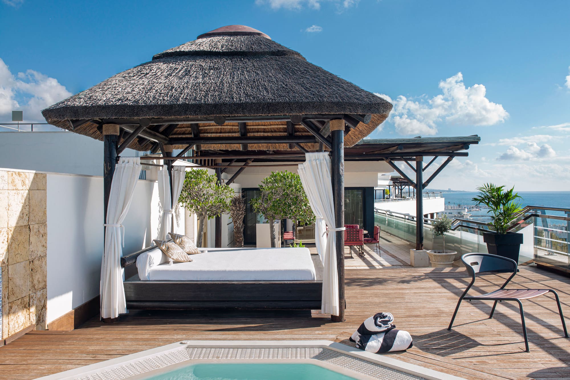 Luxury rooftop terrace with thatched gazebo daybed, hot tub, and ocean view.