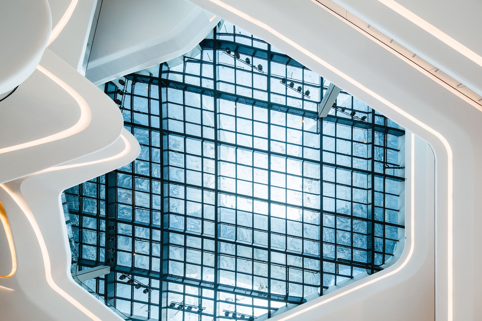 Modern white curved interior, illuminated edges, grid glass skylight.