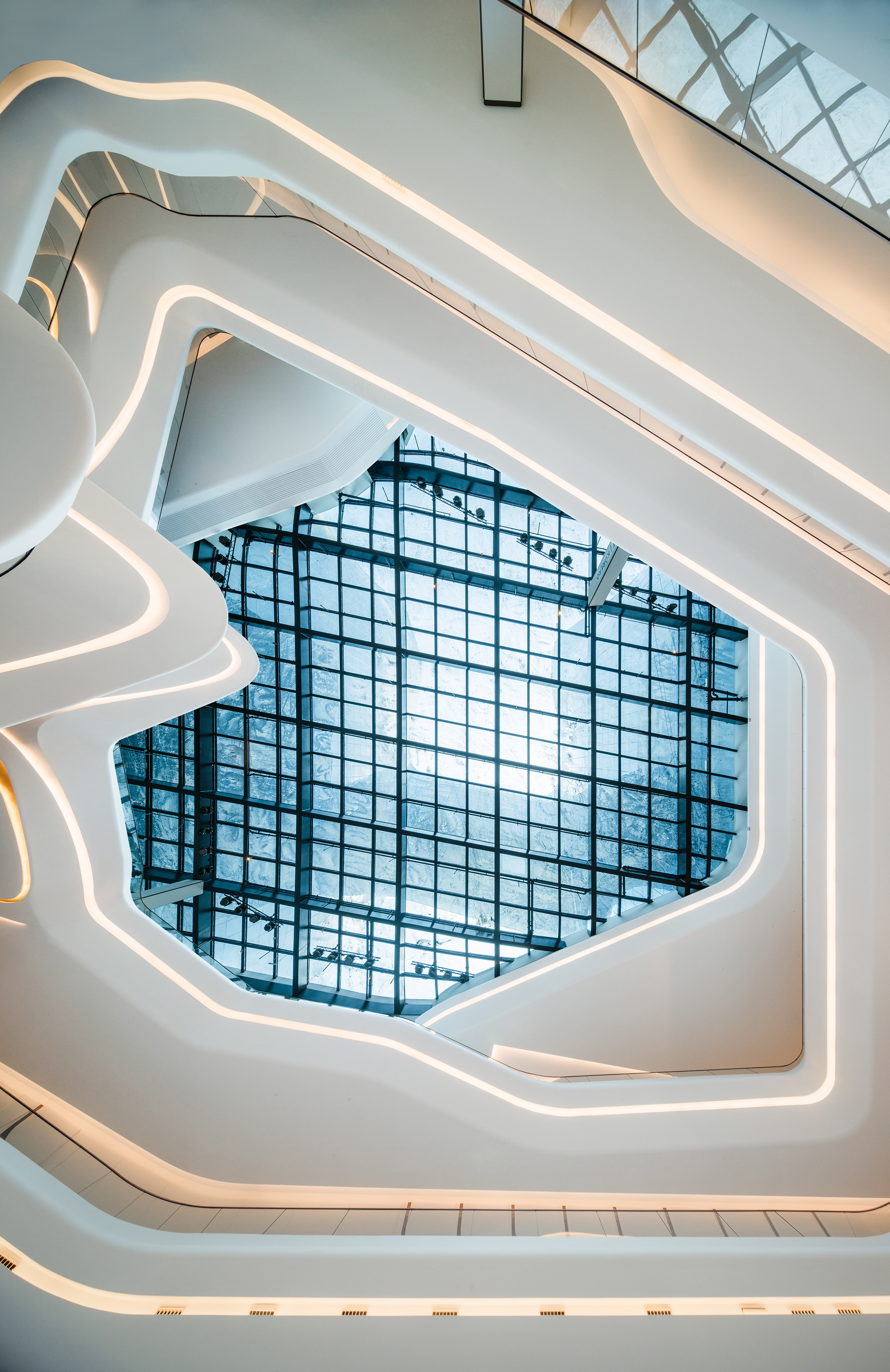 Modern white curved interior, illuminated edges, grid glass skylight.
