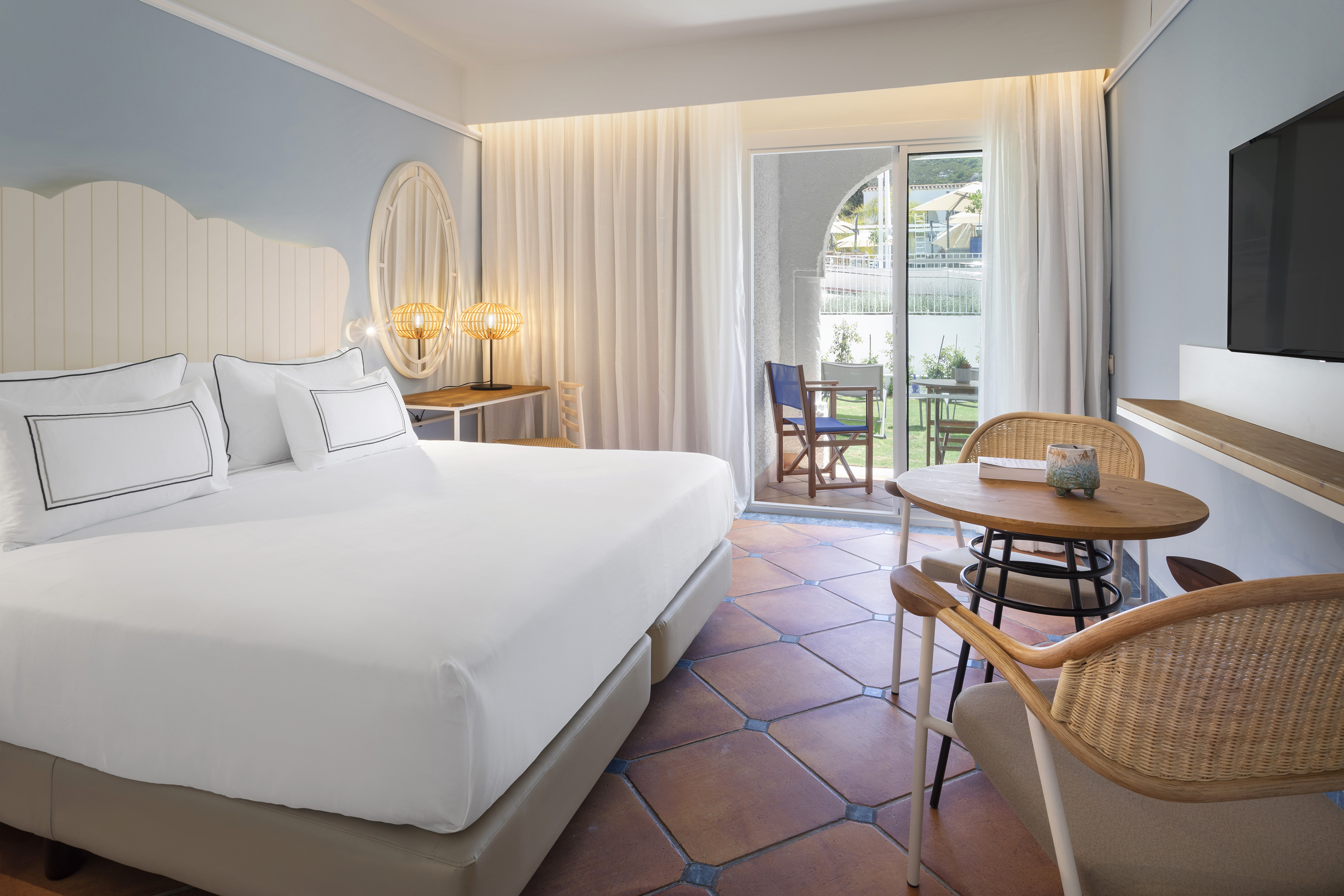 Hotel bedroom with white king bed, terracotta floor, and patio access.