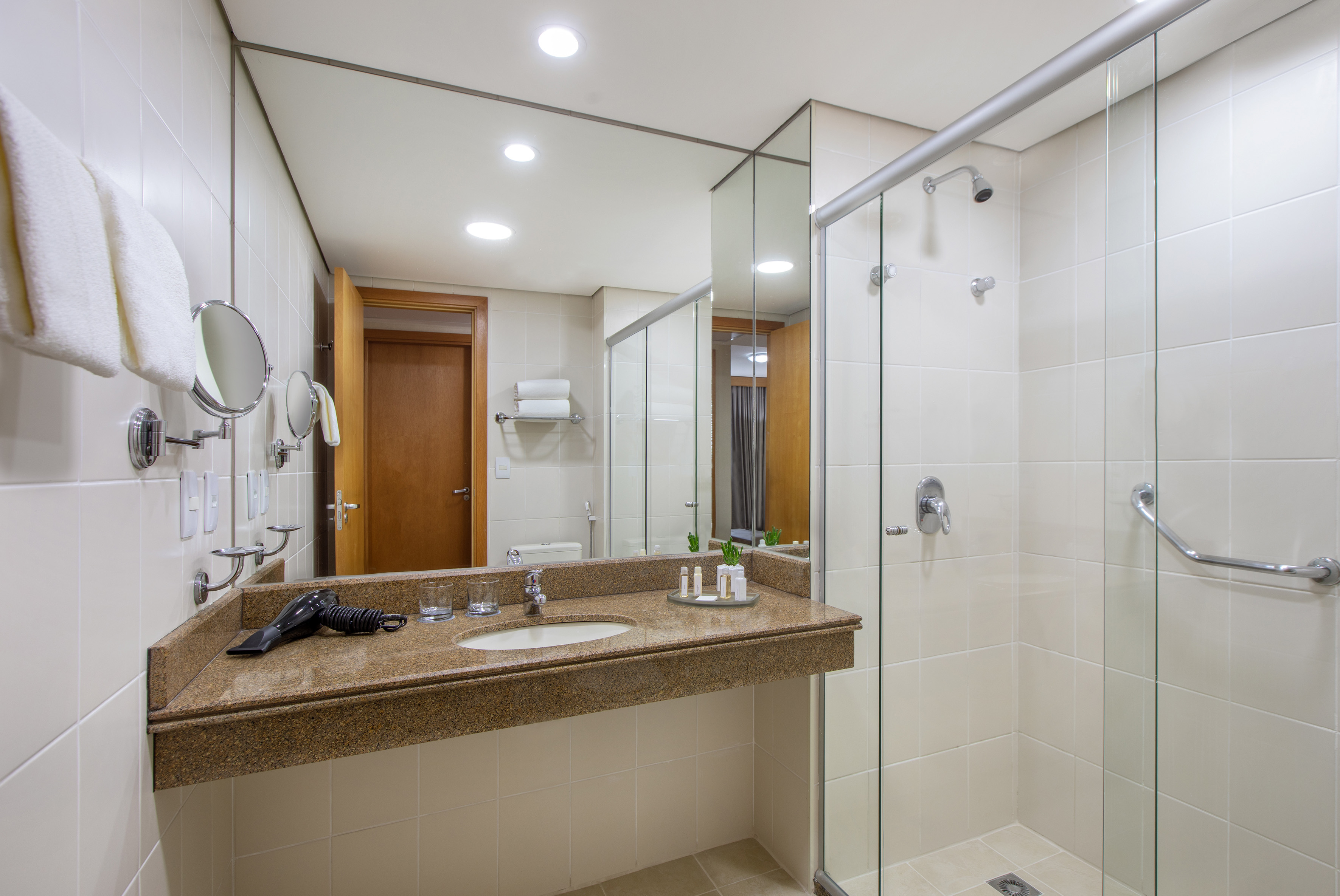 Modern hotel bathroom with granite vanity, sink, mirror, and glass shower.