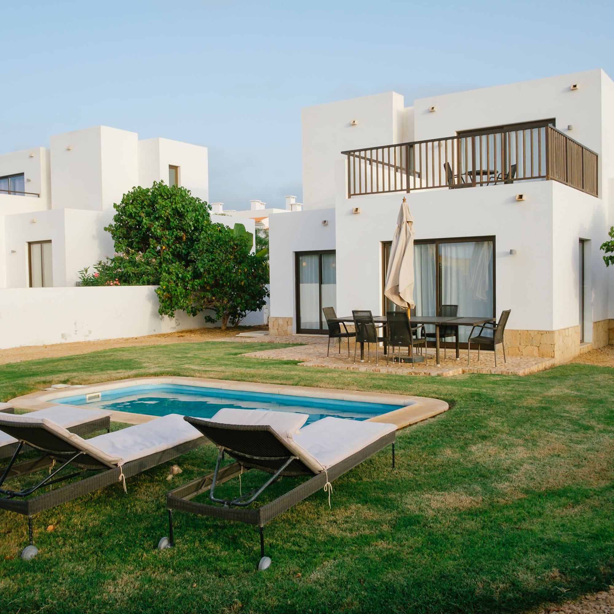 a pool in a yard with chairs in front of a house