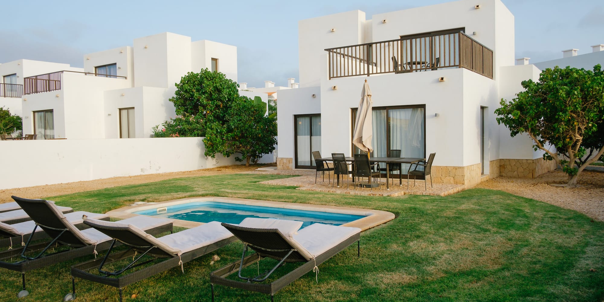 a pool in a yard with chairs in front of a house