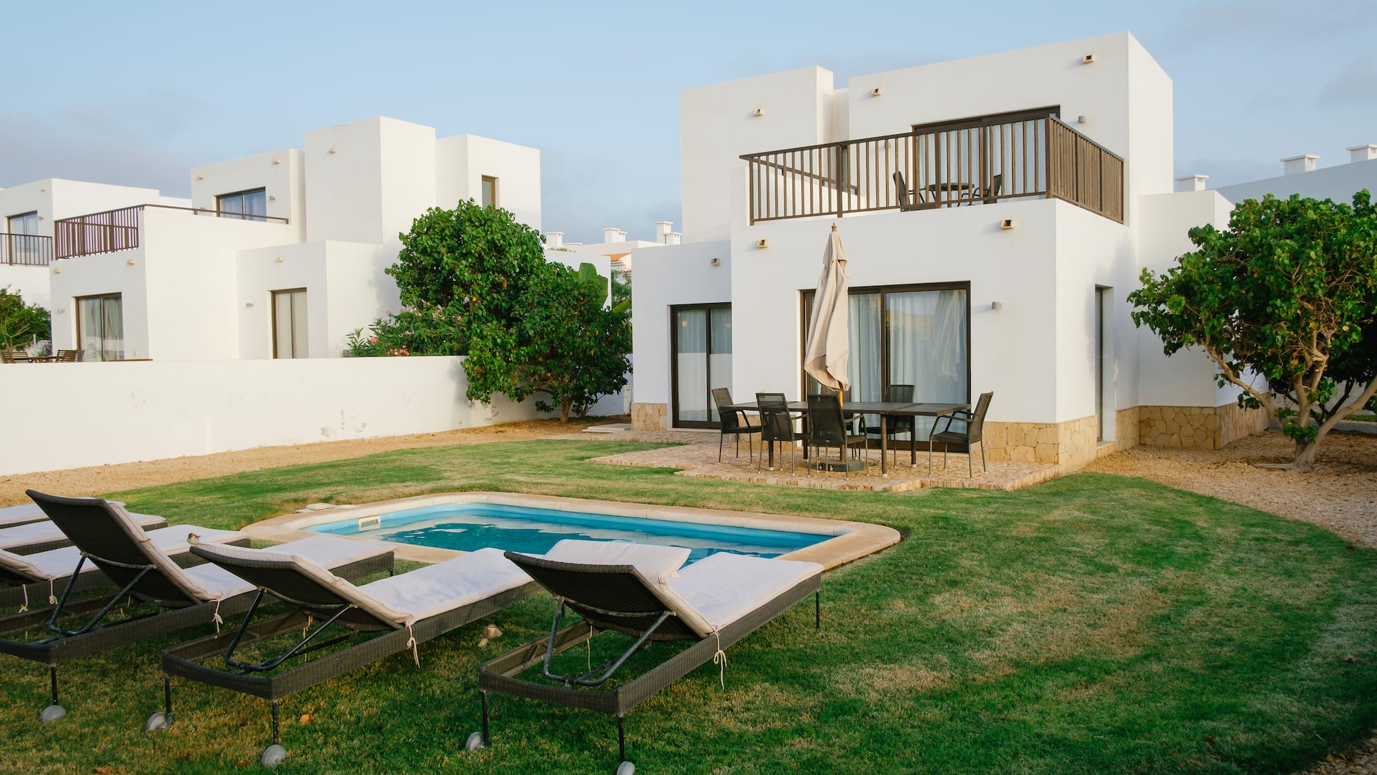 a pool in a yard with chairs in front of a house