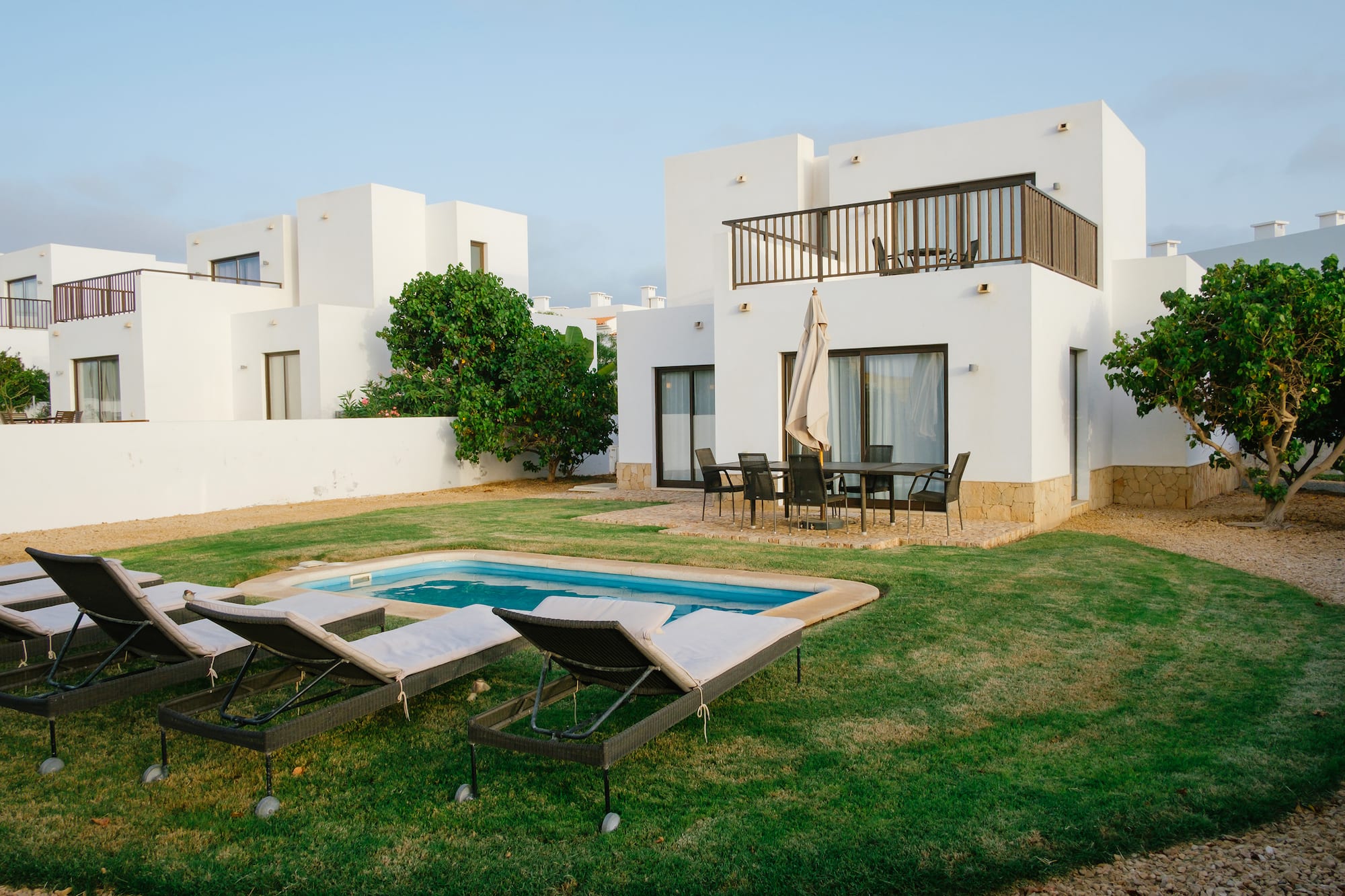 a pool in a yard with chairs in front of a house