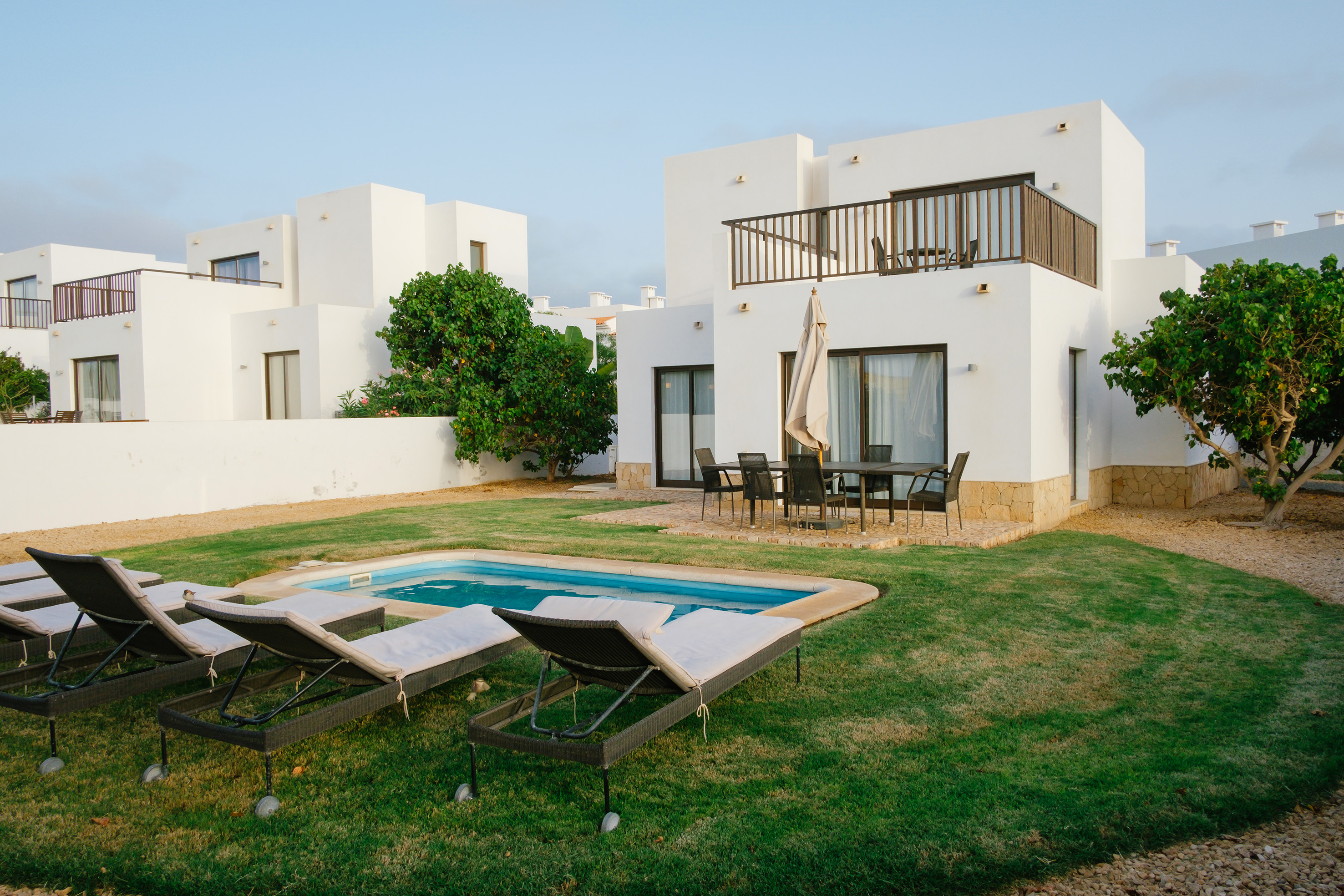 a pool in a yard with chairs in front of a house