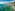 Aerial view of a coastal town bay with boats, sandy beach, and green mountains.