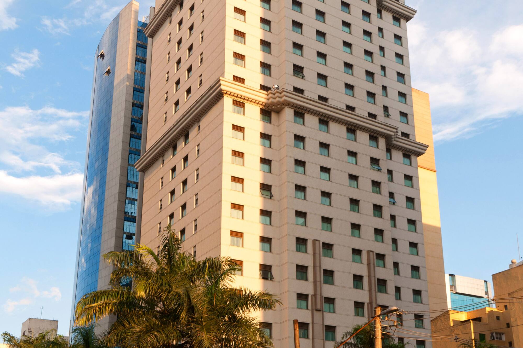 Cream high-rise building, glass skyscraper, palm trees, city street with people.