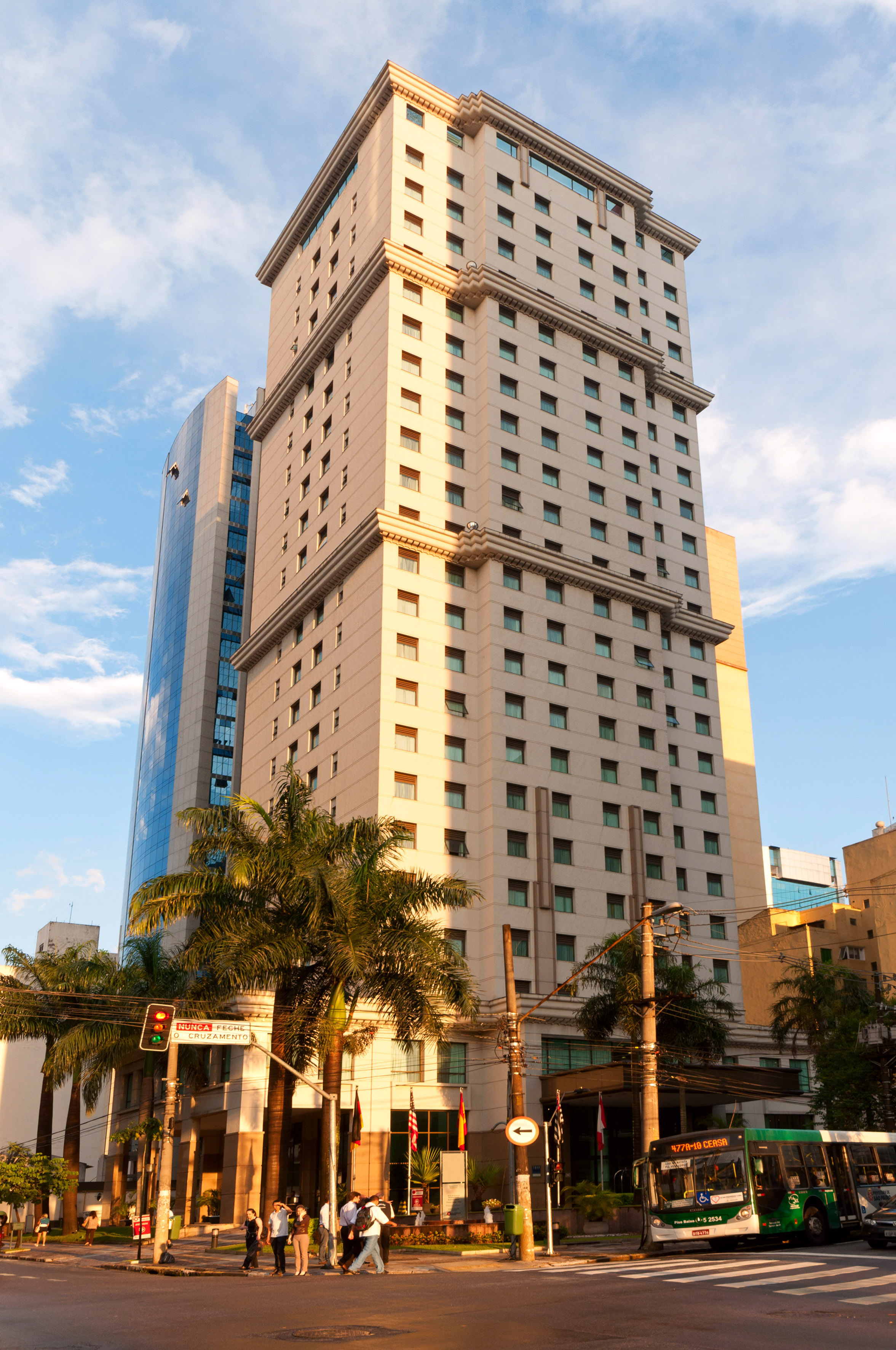 Cream high-rise building, glass skyscraper, palm trees, city street with people.