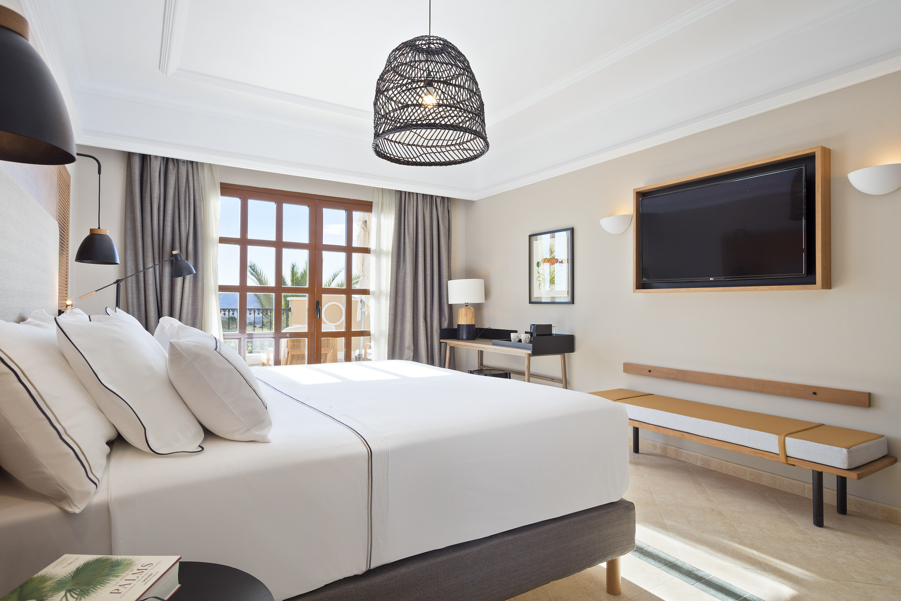 Luxury hotel bedroom with large bed, balcony, TV, and modern furnishings.