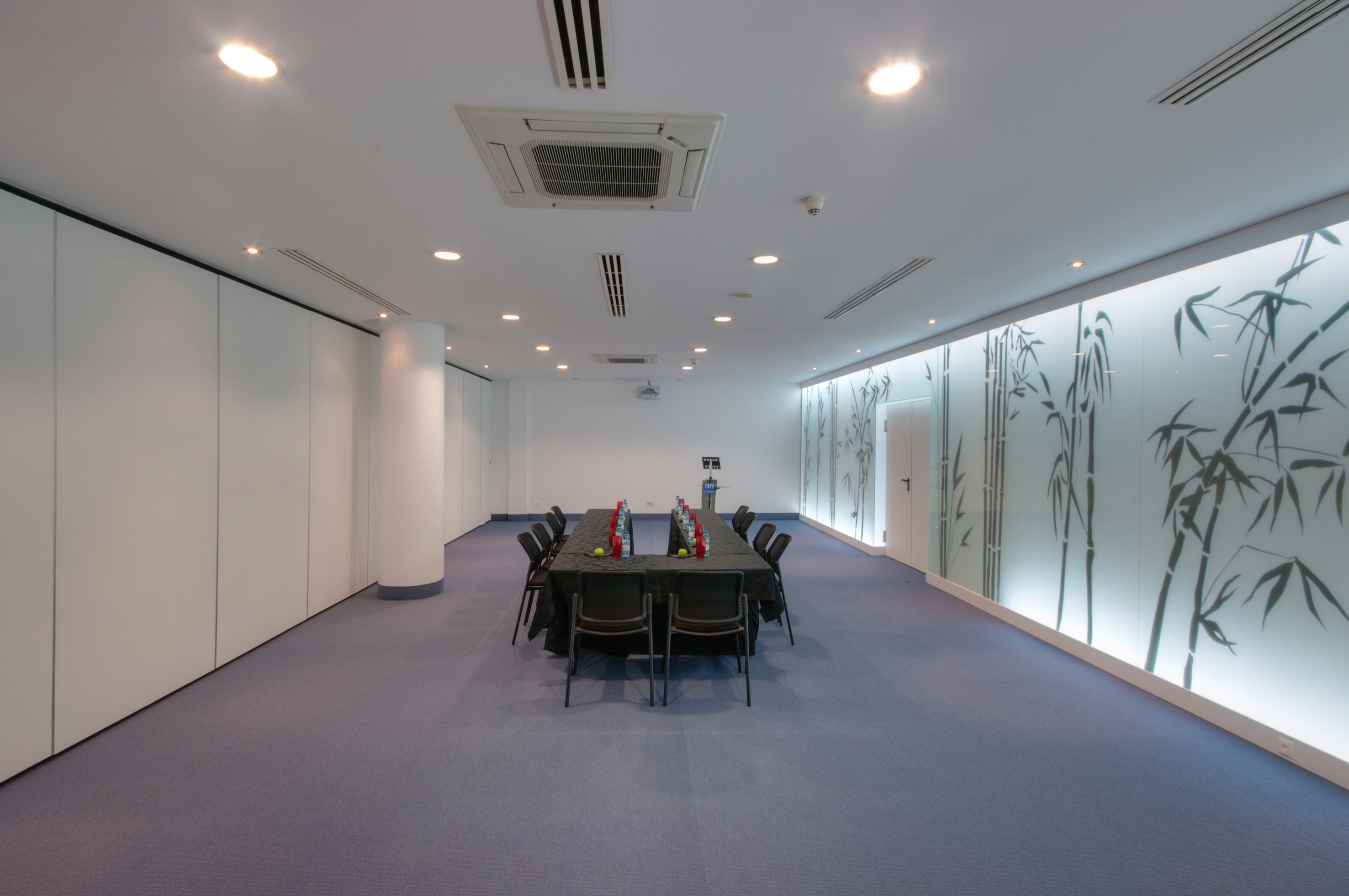 Modern conference room, black table, blue carpet, backlit bamboo wall.