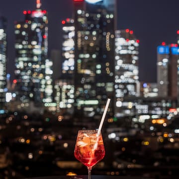 a glass of red liquid with a straw in front of a city skyline